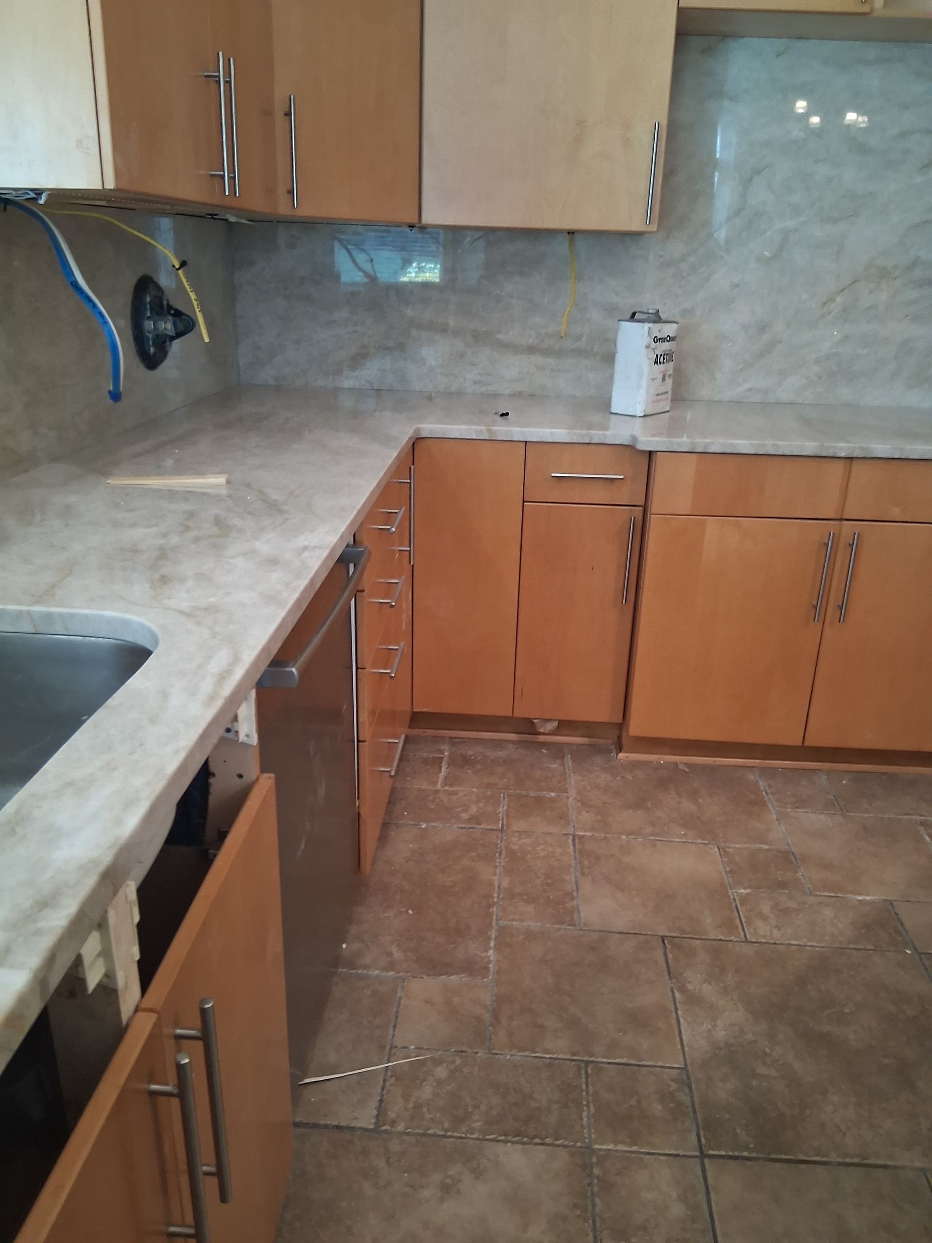 Empty kitchen with wooden cabinets, beige countertops, and brown tiled floor.
