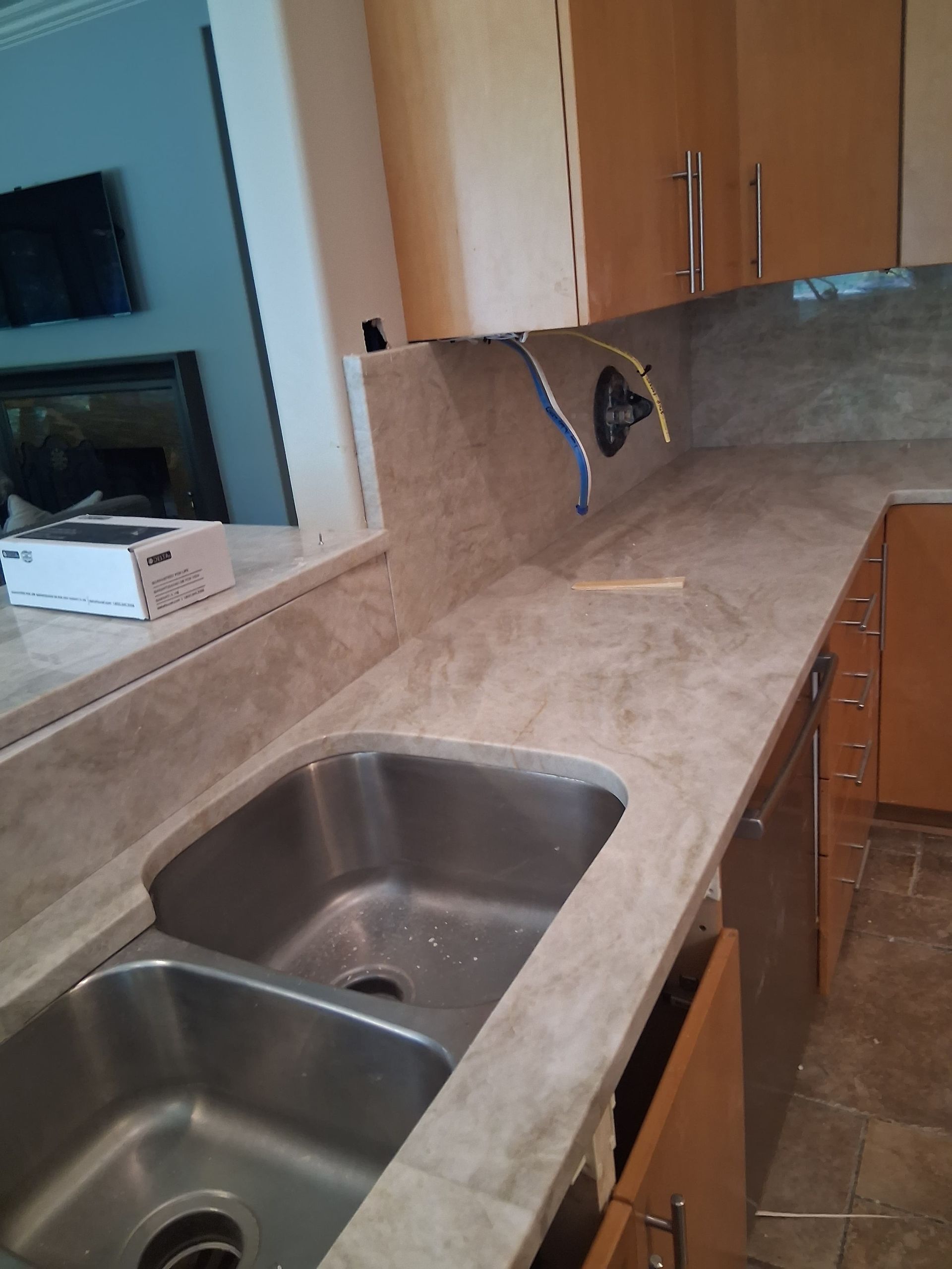 Kitchen countertop with double stainless steel sink and beige tile backsplash under wooden cabinets