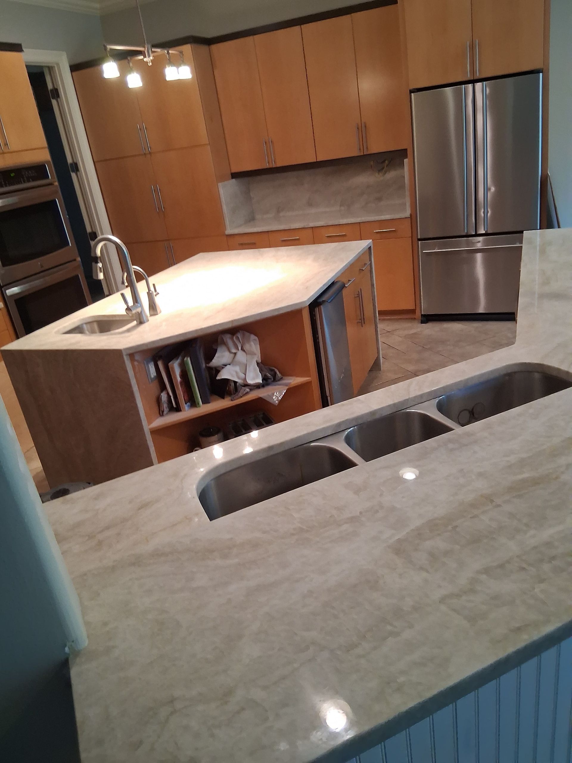 Modern kitchen with wood cabinets, granite island, double sink, and stainless steel refrigerator.