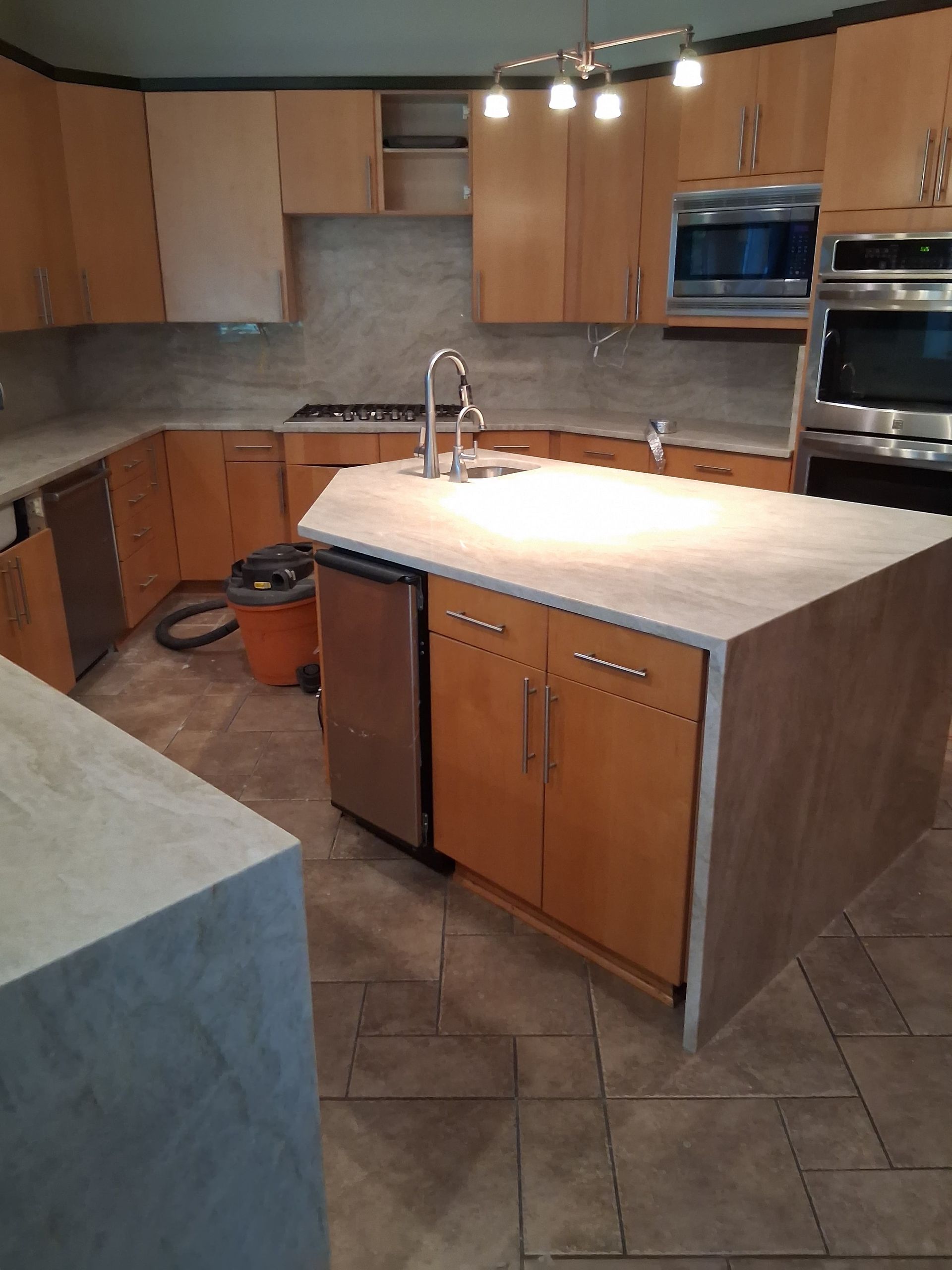 Modern kitchen with wood cabinets, tiled floor, and a large island with sink and light stone countertop.