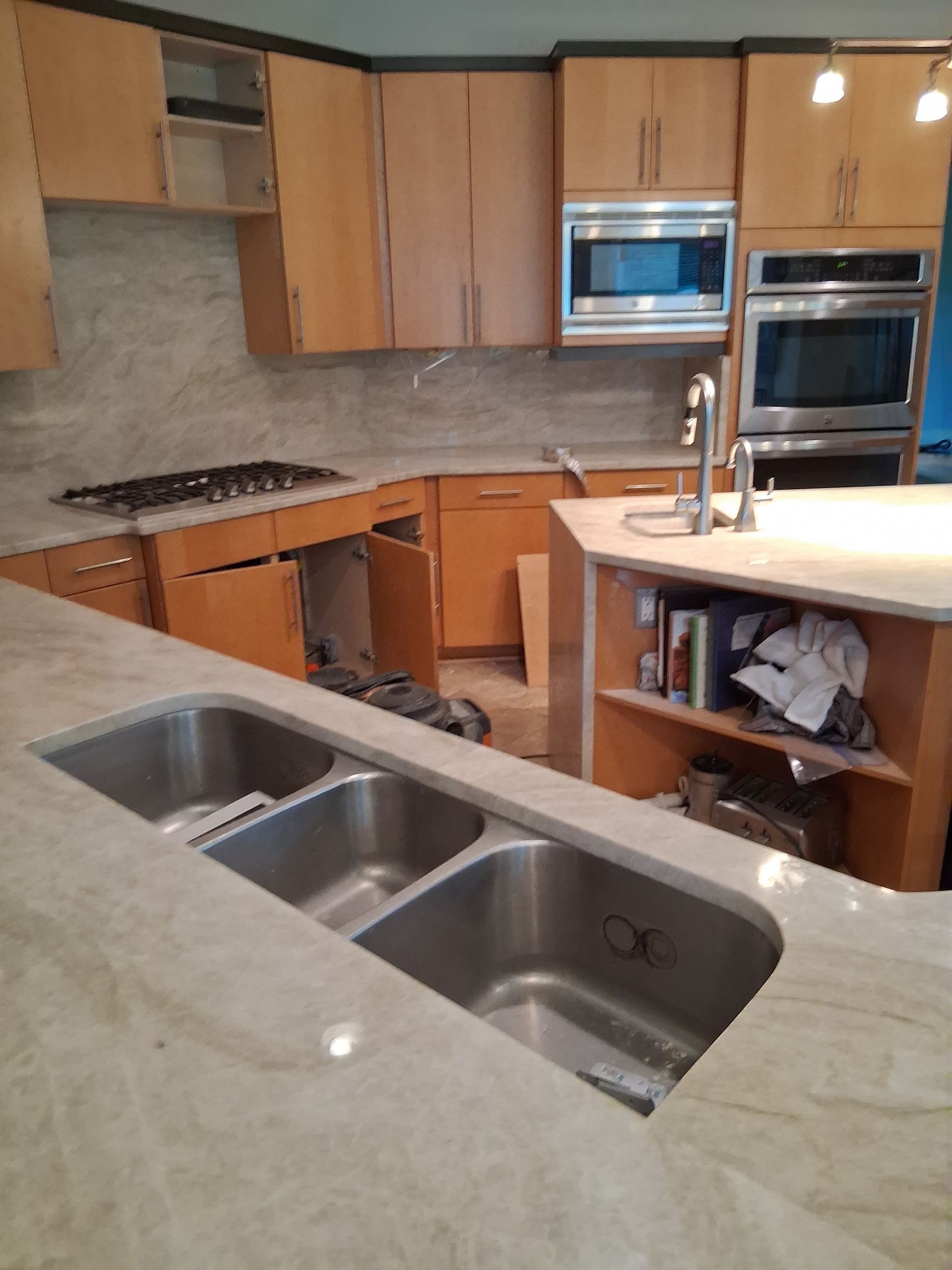 Modern kitchen with granite island, stainless sink, wood cabinets, and built-in oven and microwave.
