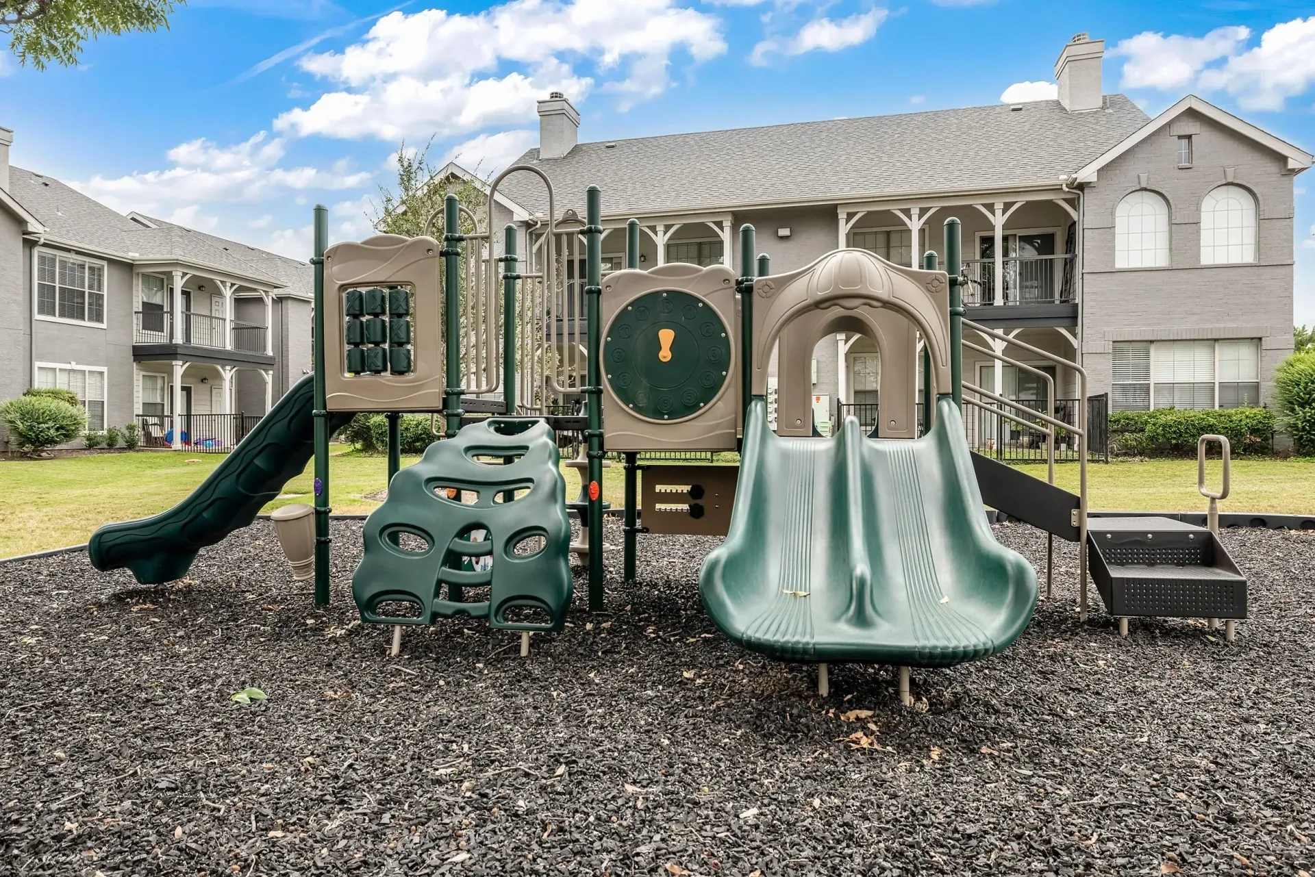 Playground equipment with slides and climbing structures in front of apartment buildings.