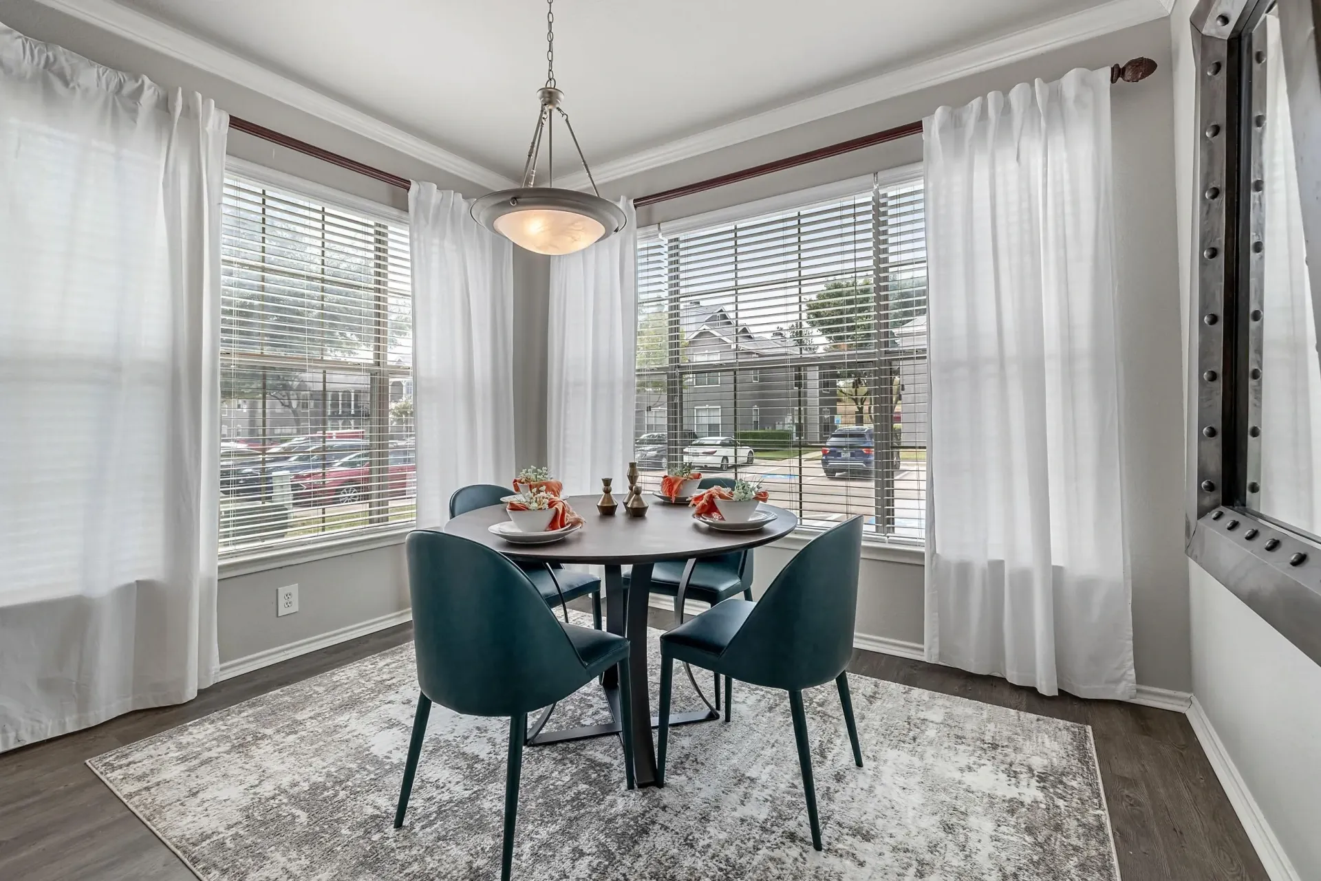 Dining room with a round table and four teal chairs set near large windows.