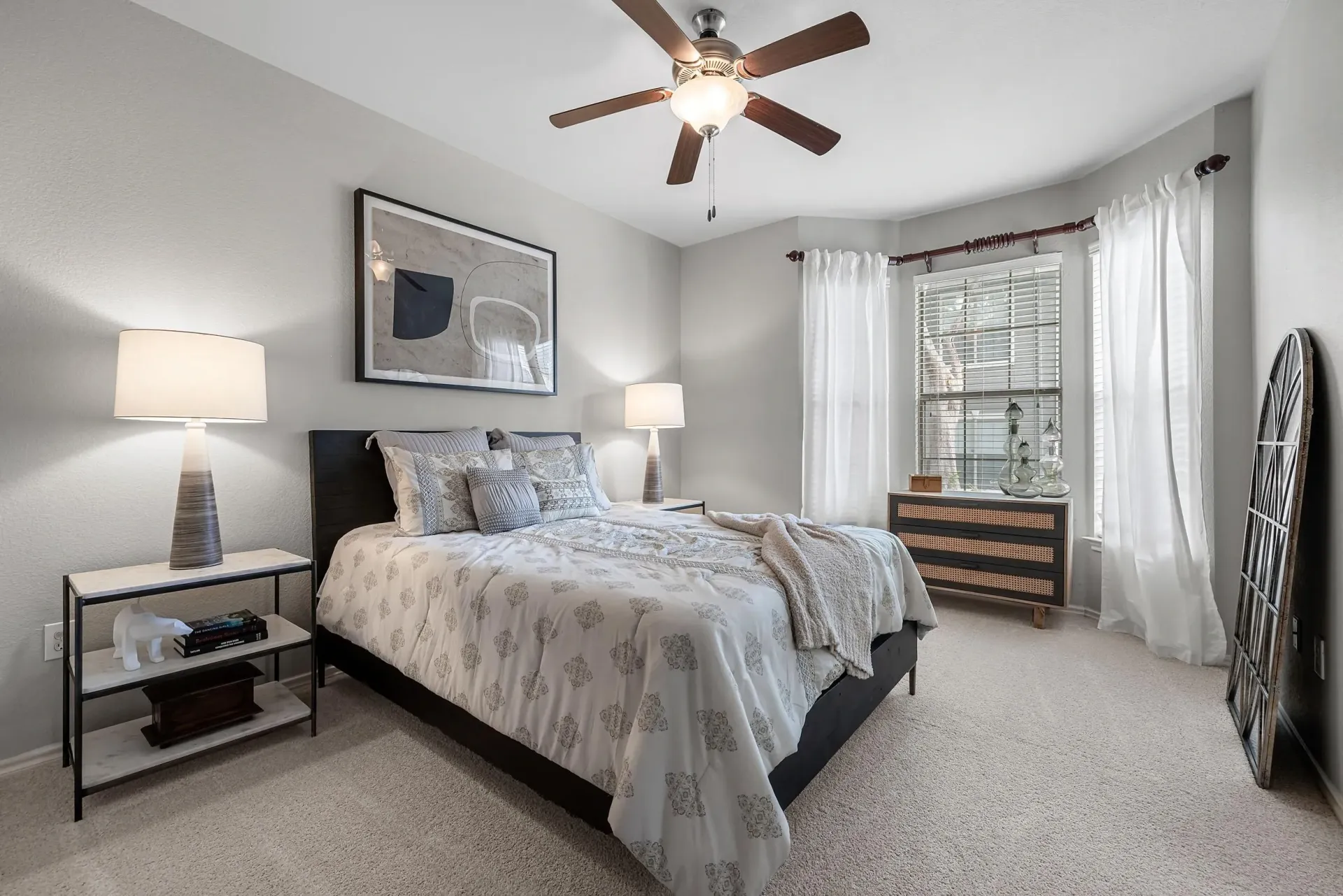 A bedroom with a bed, nightstand, dresser, and fan.
