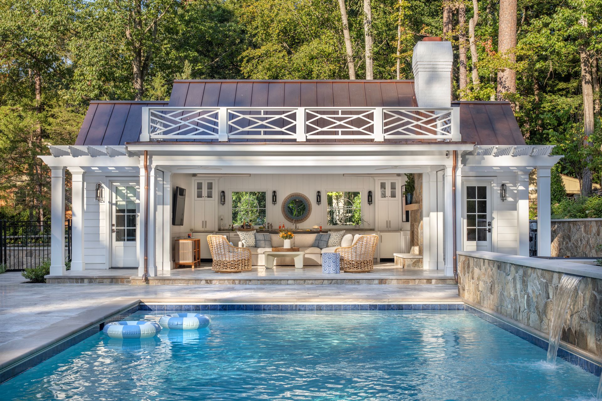 Poolside cabana with white pergola, copper roof, pool, and surrounding trees.