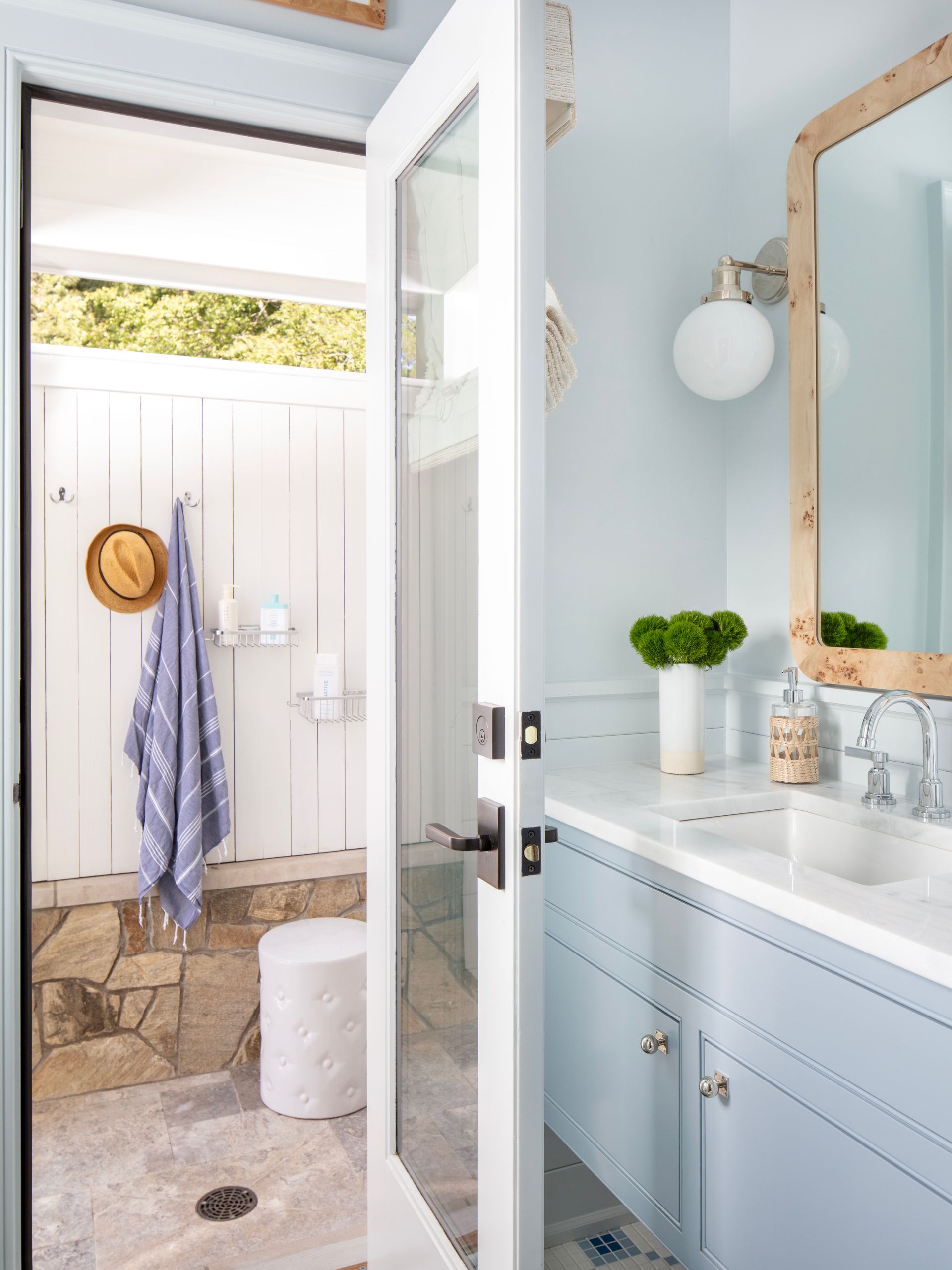 Bathroom with open door to outdoor shower; light blue walls, marble vanity, stone floor, and white door.