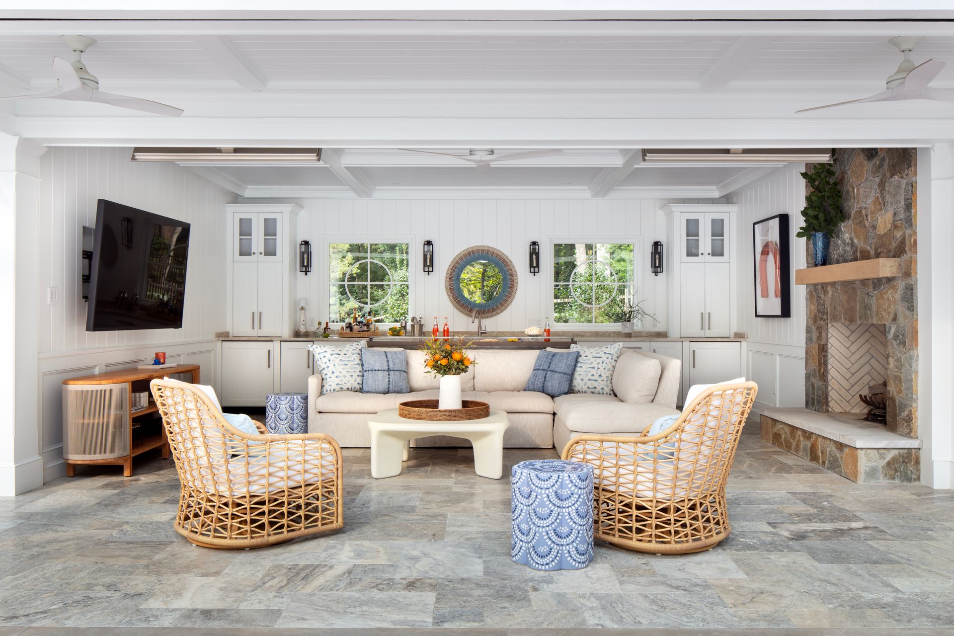 Outdoor living space with sofa, chairs, TV, fireplace, and built-in white cabinets.