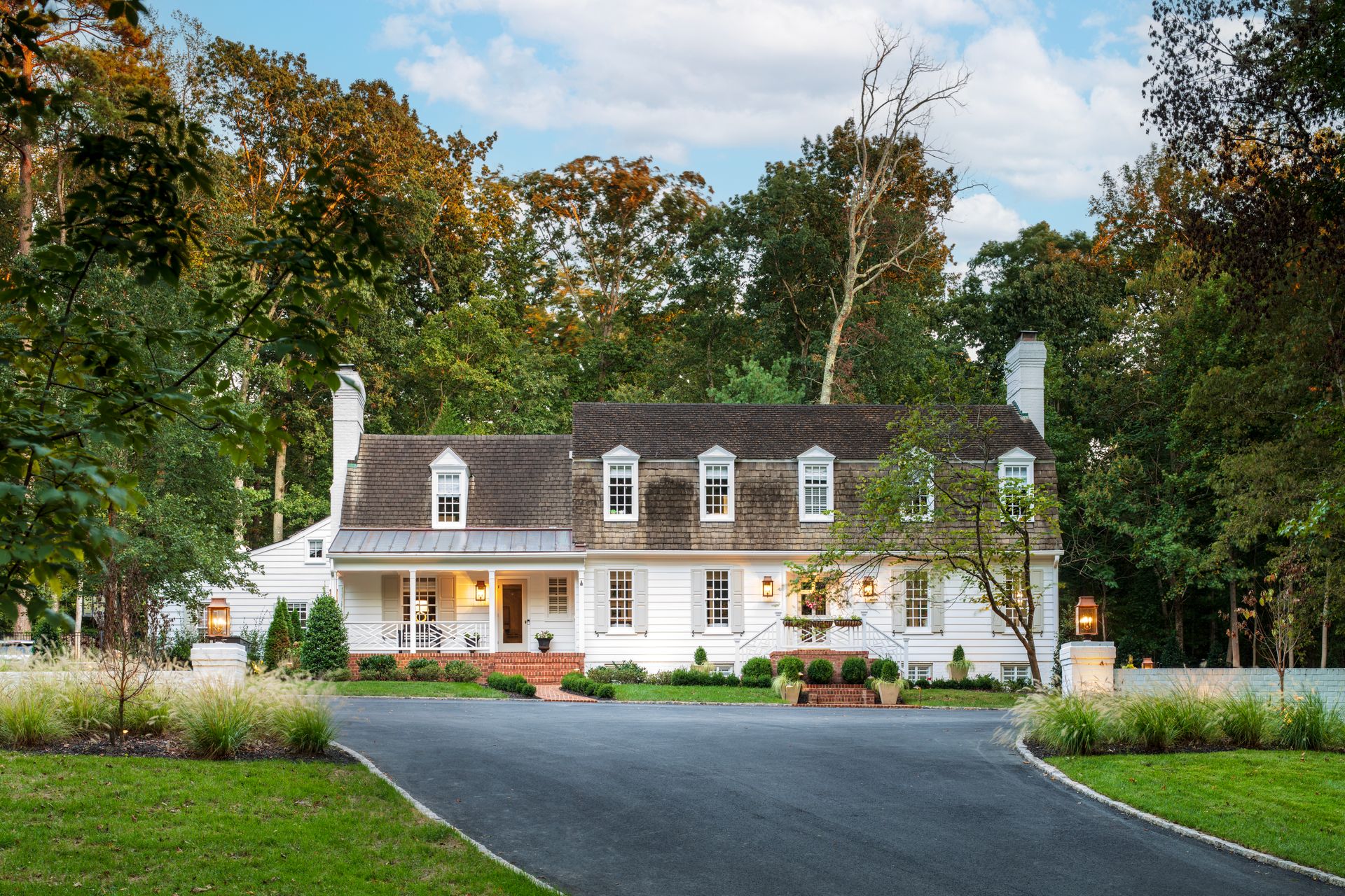 White colonial house with a long driveway surrounded by lush trees and greenery.