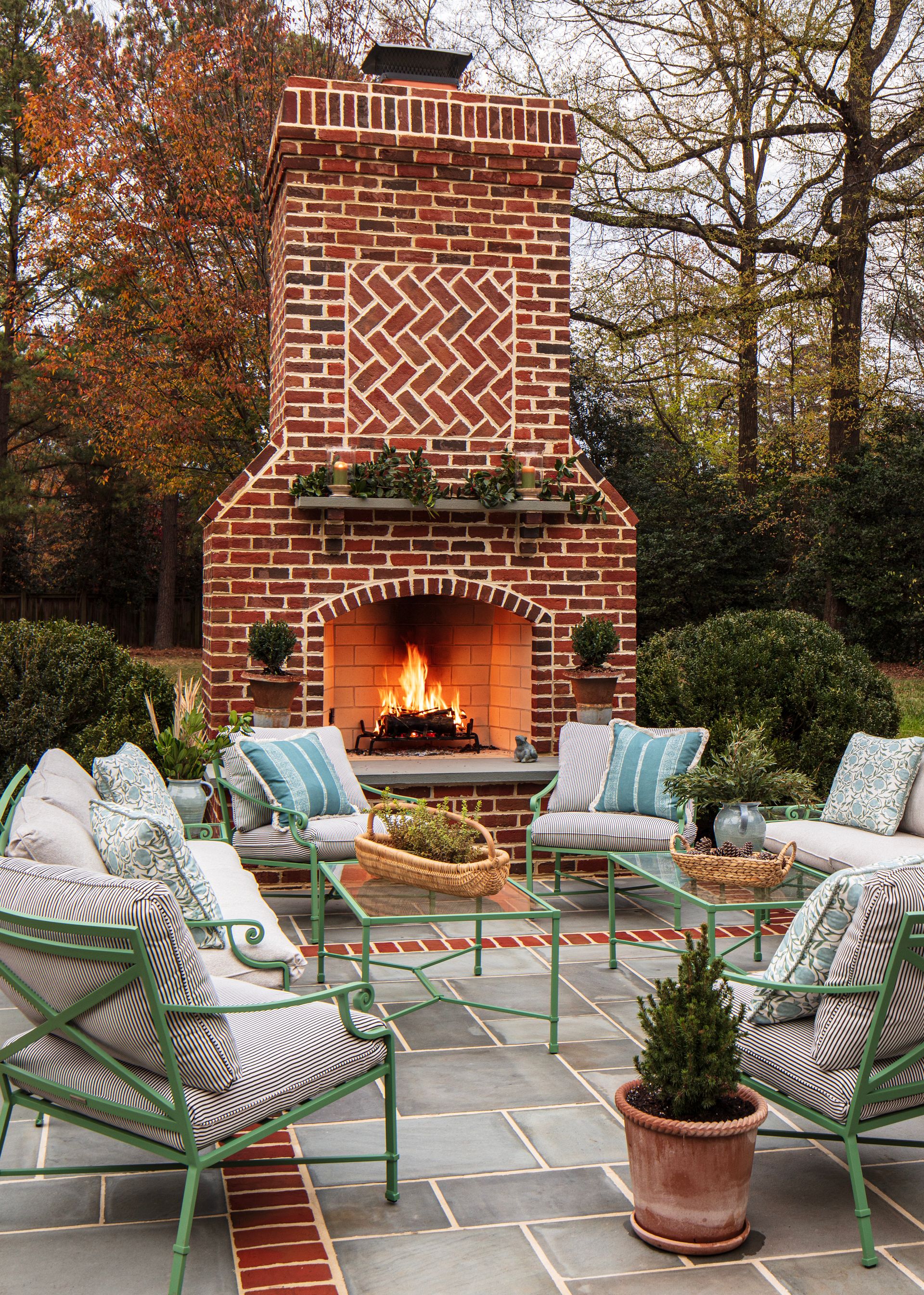 Brick outdoor fireplace with seating area; fire burning, green chairs, and patterned cushions.
