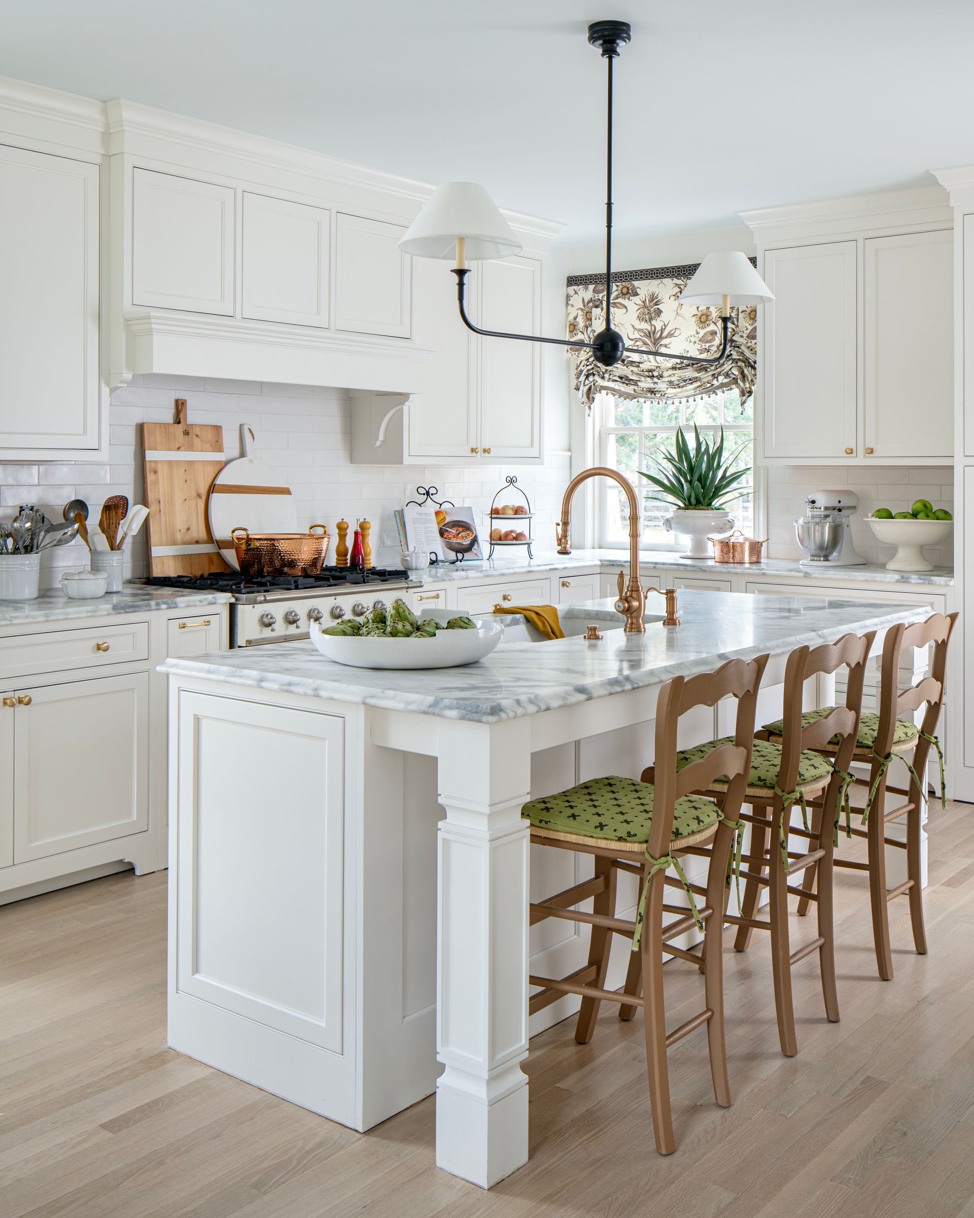 White kitchen with island, marble countertop, wooden bar stools with green patterned cushions.