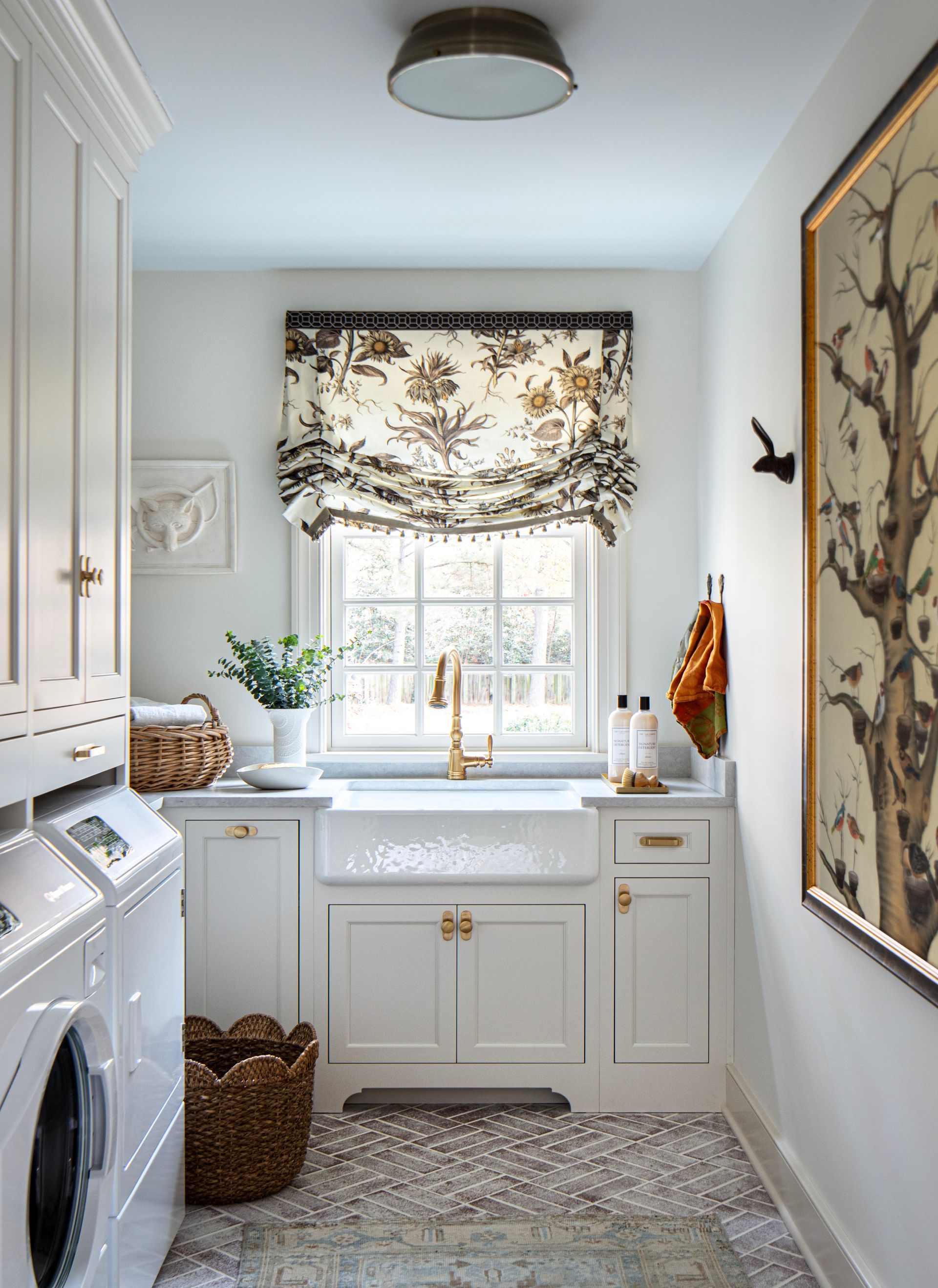 Laundry room with white cabinets, farmhouse sink, floral window shade, and patterned floor.