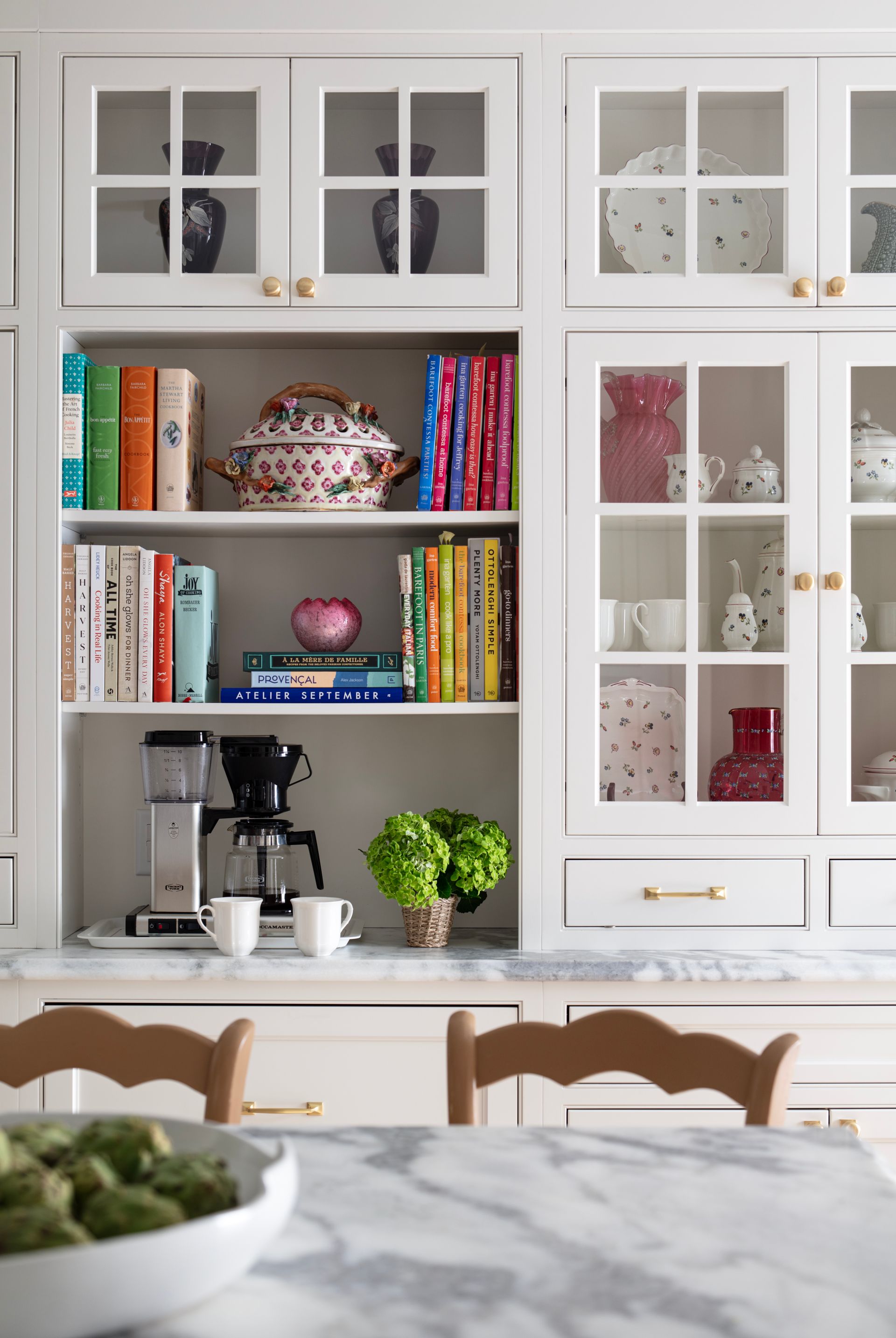 White kitchen cabinetry with glass doors, books, and decorative items.