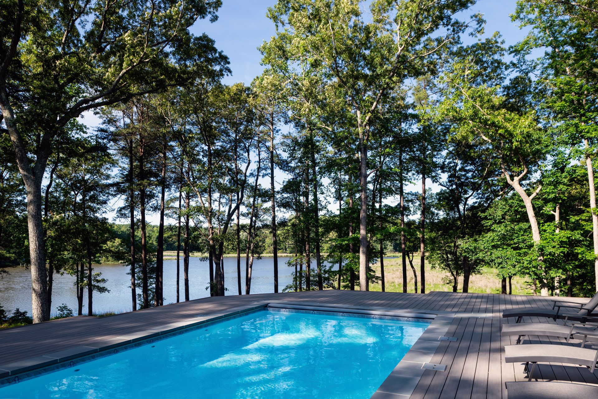 A large swimming pool surrounded by trees with a lake in the background