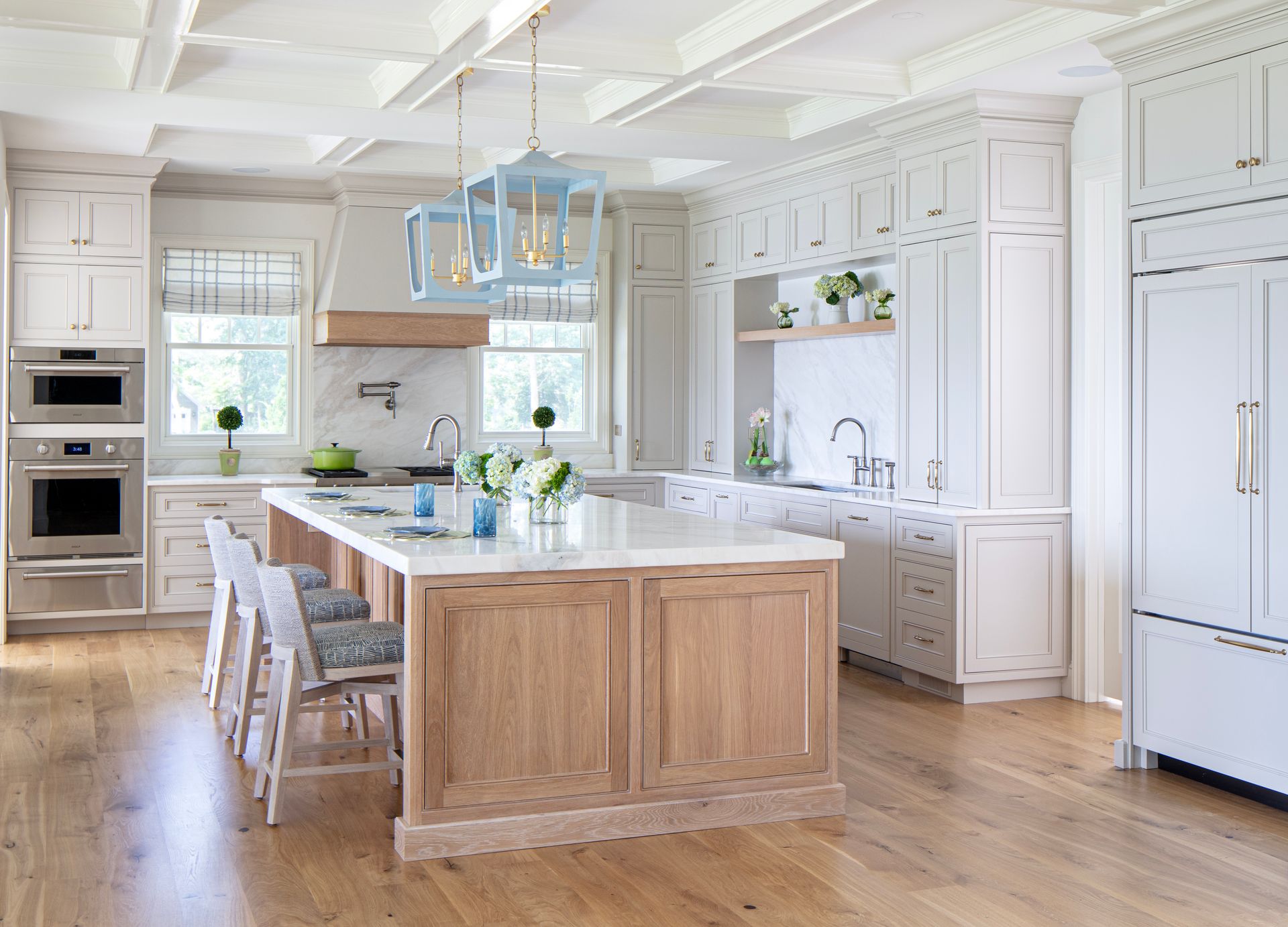 A bright, white kitchen with a large wooden island and light blue pendant lights. Stainless steel appliances and wood flooring.