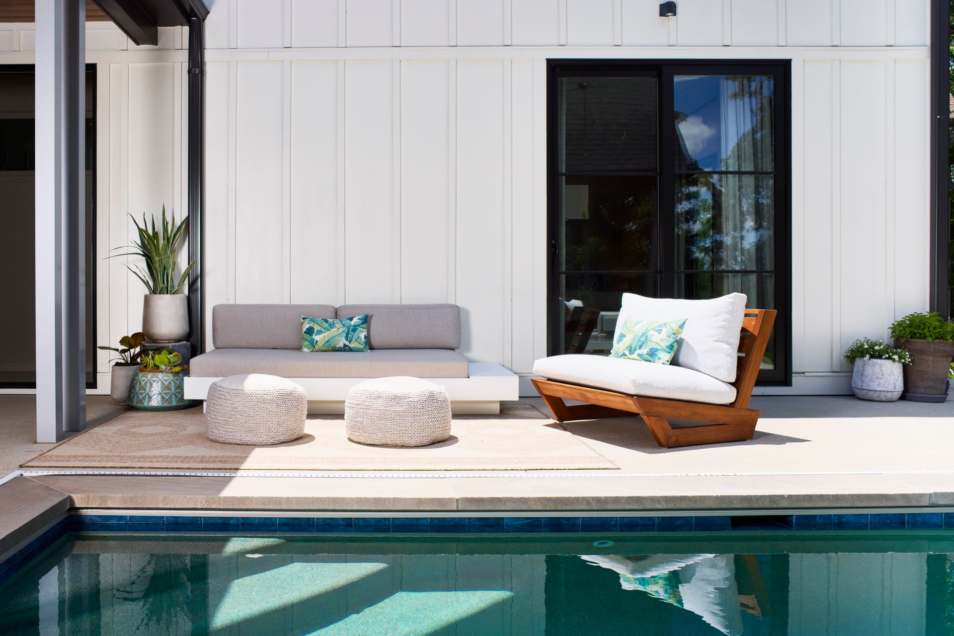 A patio with a couch and chair next to a swimming pool.