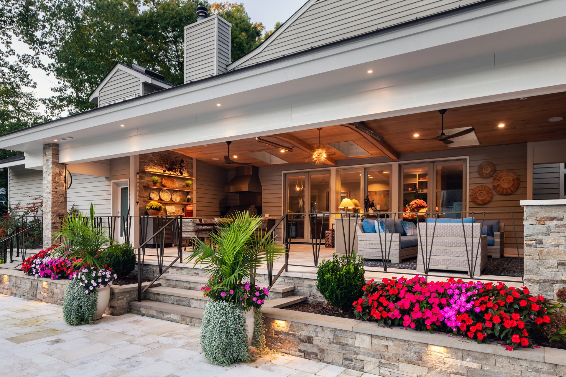 Cozy covered patio with warm lights, wooden seating, and bright pink flowers in front of a house