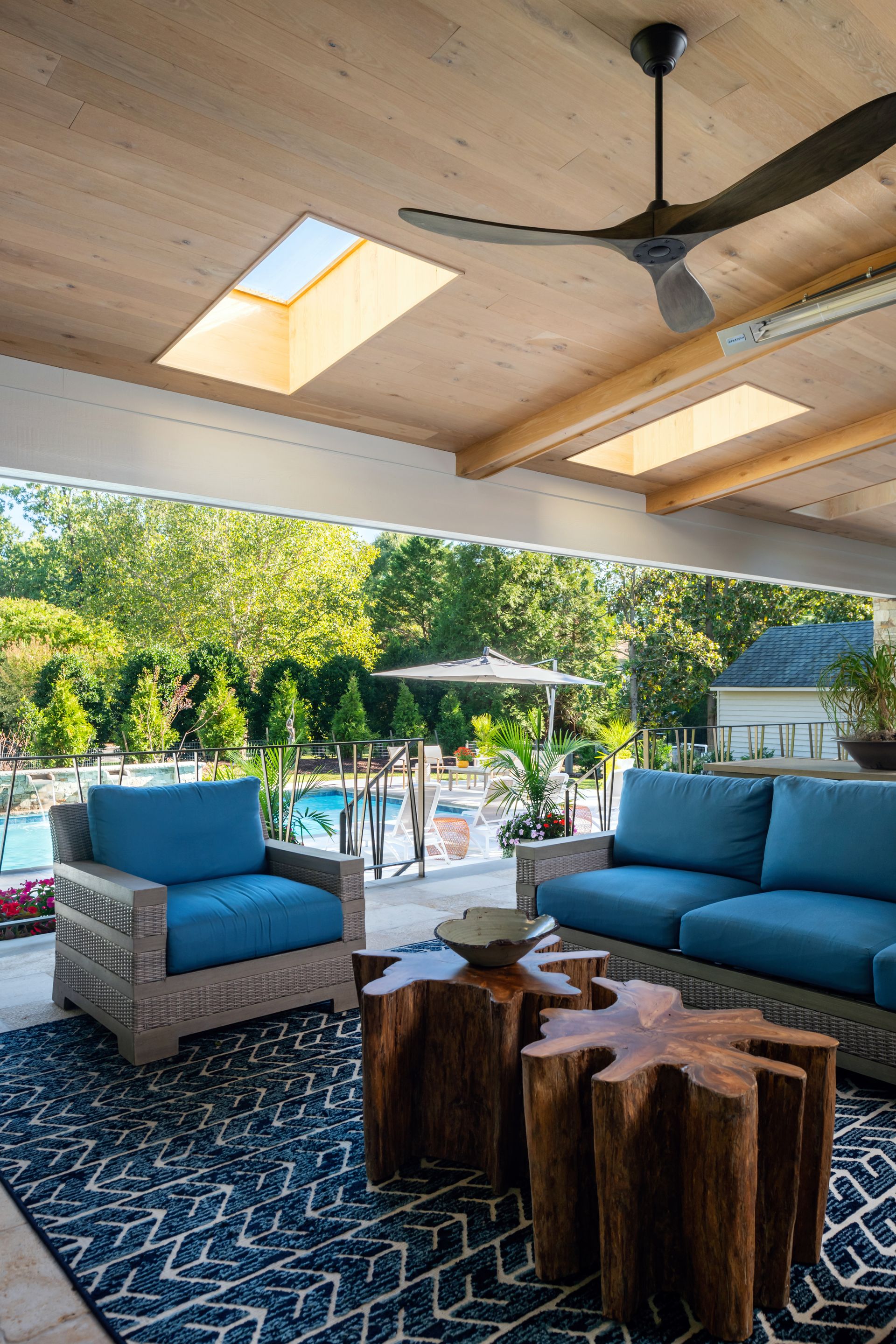 Covered patio seating with blue chairs, wood table, ceiling fan, and pool view beyond