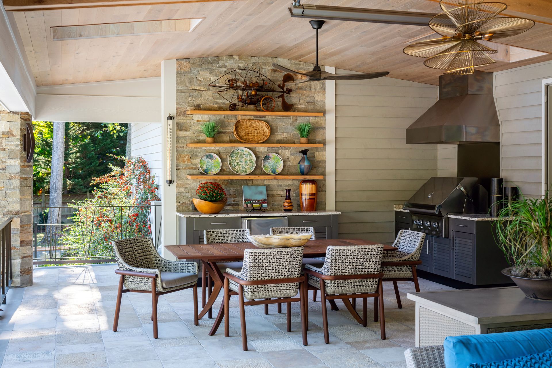 Modern patio dining area with wood shelves, patterned chairs, fireplace, and open view to the garden