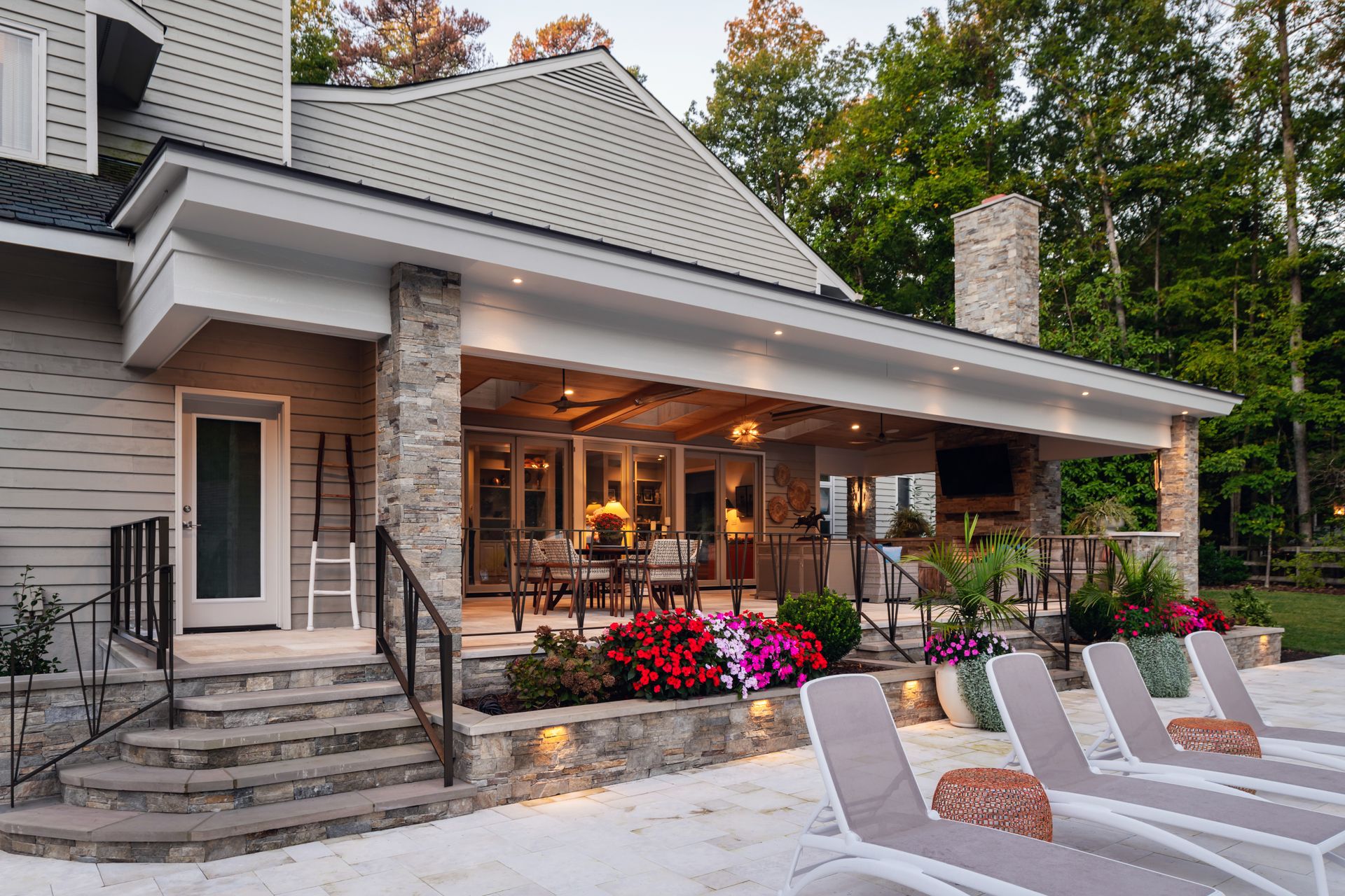 Stone house with a covered patio, flowering planters, and lounge chairs beside a pool at dusk