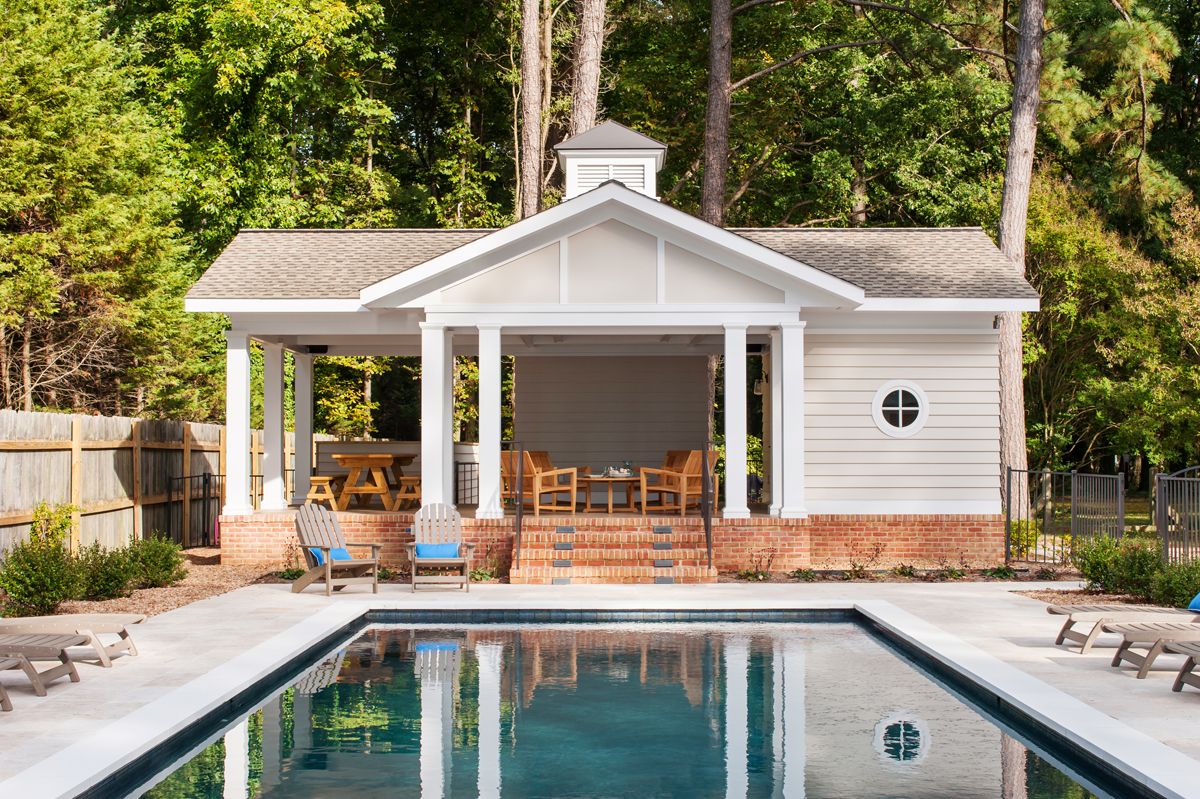 Poolside cabana with a brick base and white siding. A pool with clear blue water reflects the cabana.