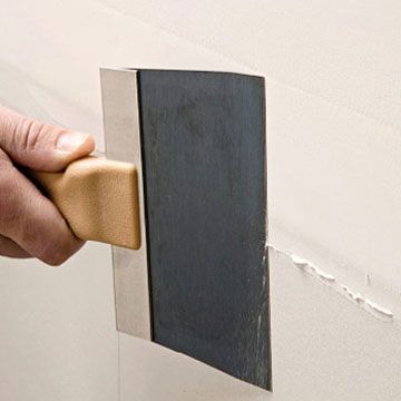 A person is holding a spatula over a white wall.