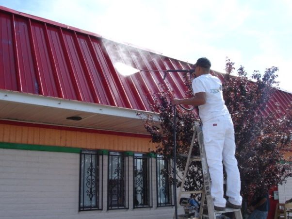 A man on a ladder cleaning a red roof