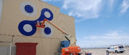 A crane is painting a large blue circle on the side of a building.
