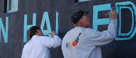 Two men are painting the word hailed on a wall