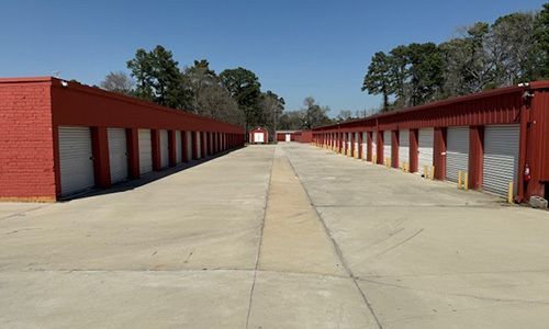 Row of red storage units along a wide concrete lane under a clear blue sky.
