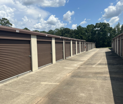 Row of brown storage unit doors along a concrete lane under a blue sky with clouds