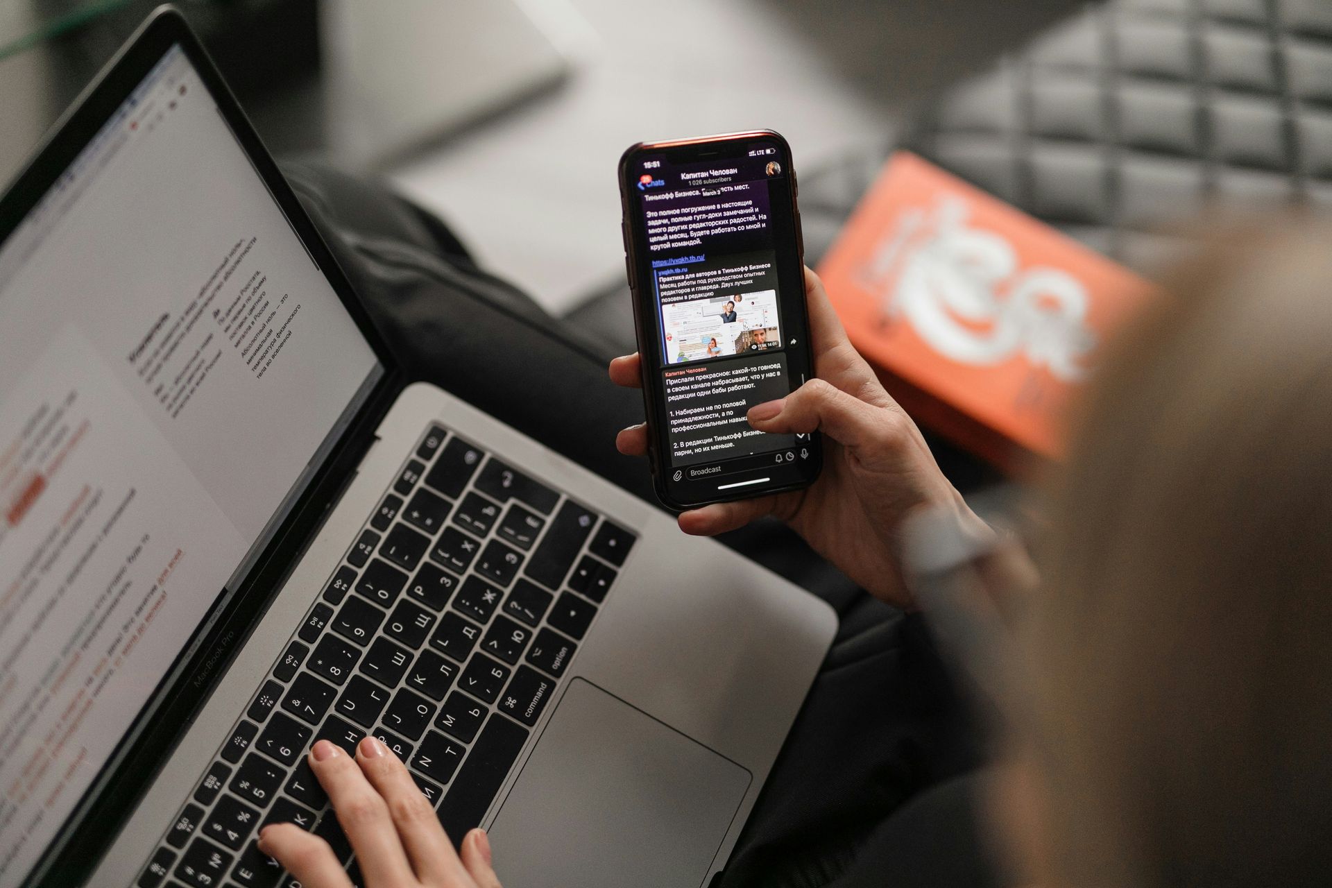 Person using laptop and smartphone simultaneously, indoors.