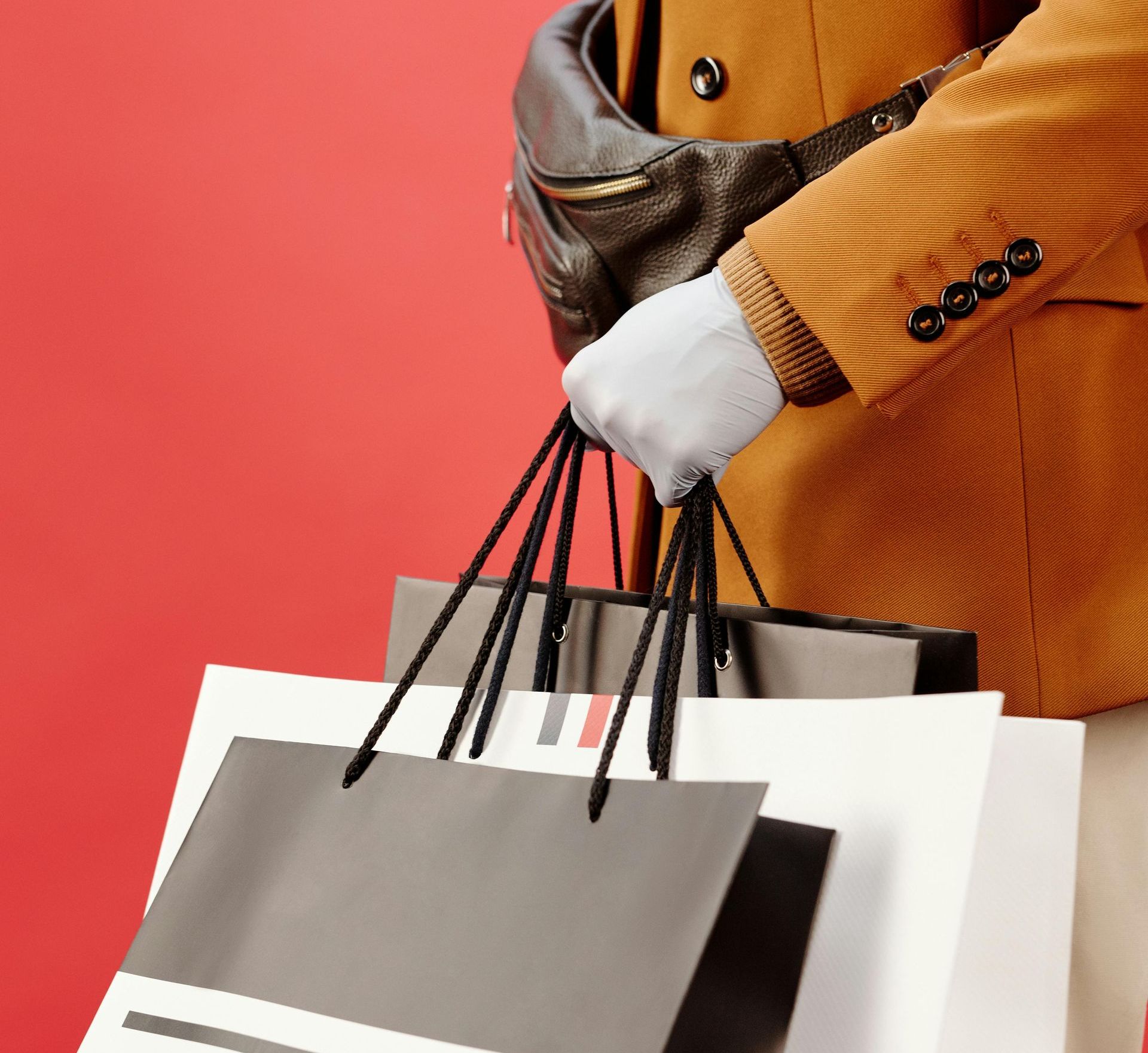 Person wearing a brown jacket holding shopping bags with black handles.