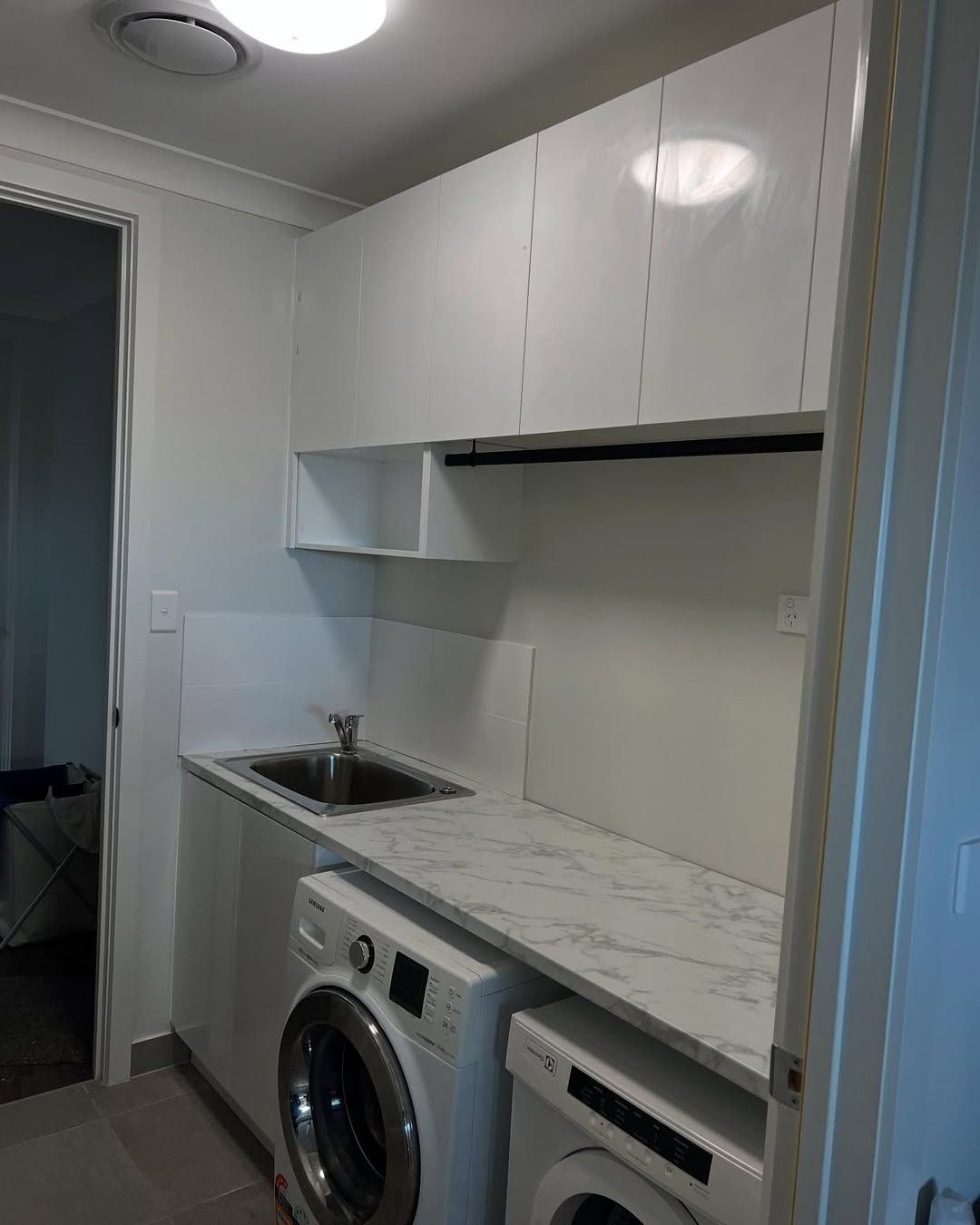 White Laundry Room With Upper Cabinets, Counter, Sink, Washing Machine, And Dryer — Protech Renovations & Joinery in Campbelltown, NSW