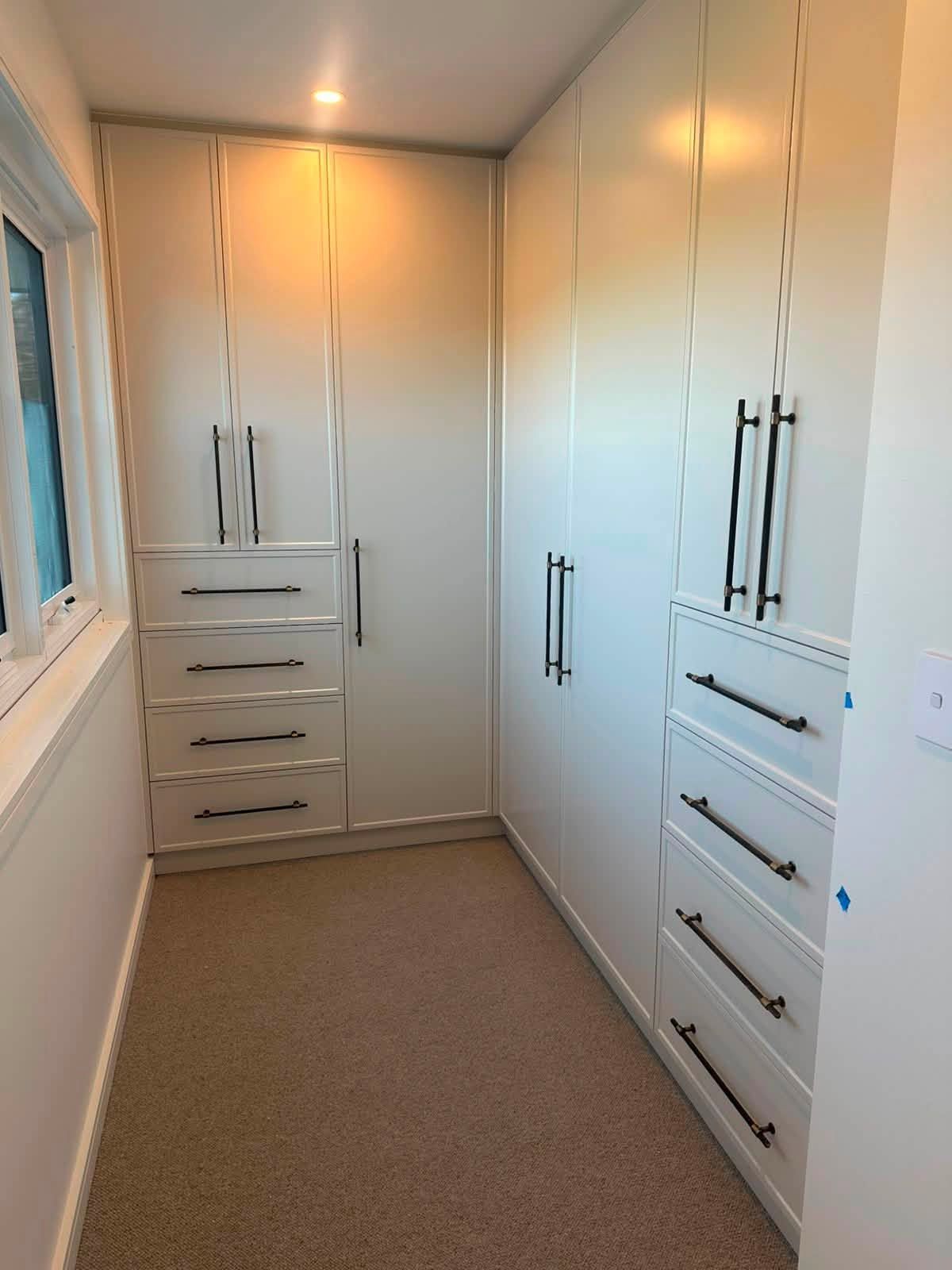 Narrow white walk-in closet with built-in cabinets and drawers along both walls. — Protech Renovations & Joinery in Gregory Hills, NSW