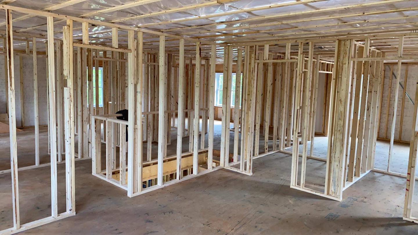 Vue intérieure d'un bâtiment en construction, montrant la charpente murale en bois et un sol en béton.