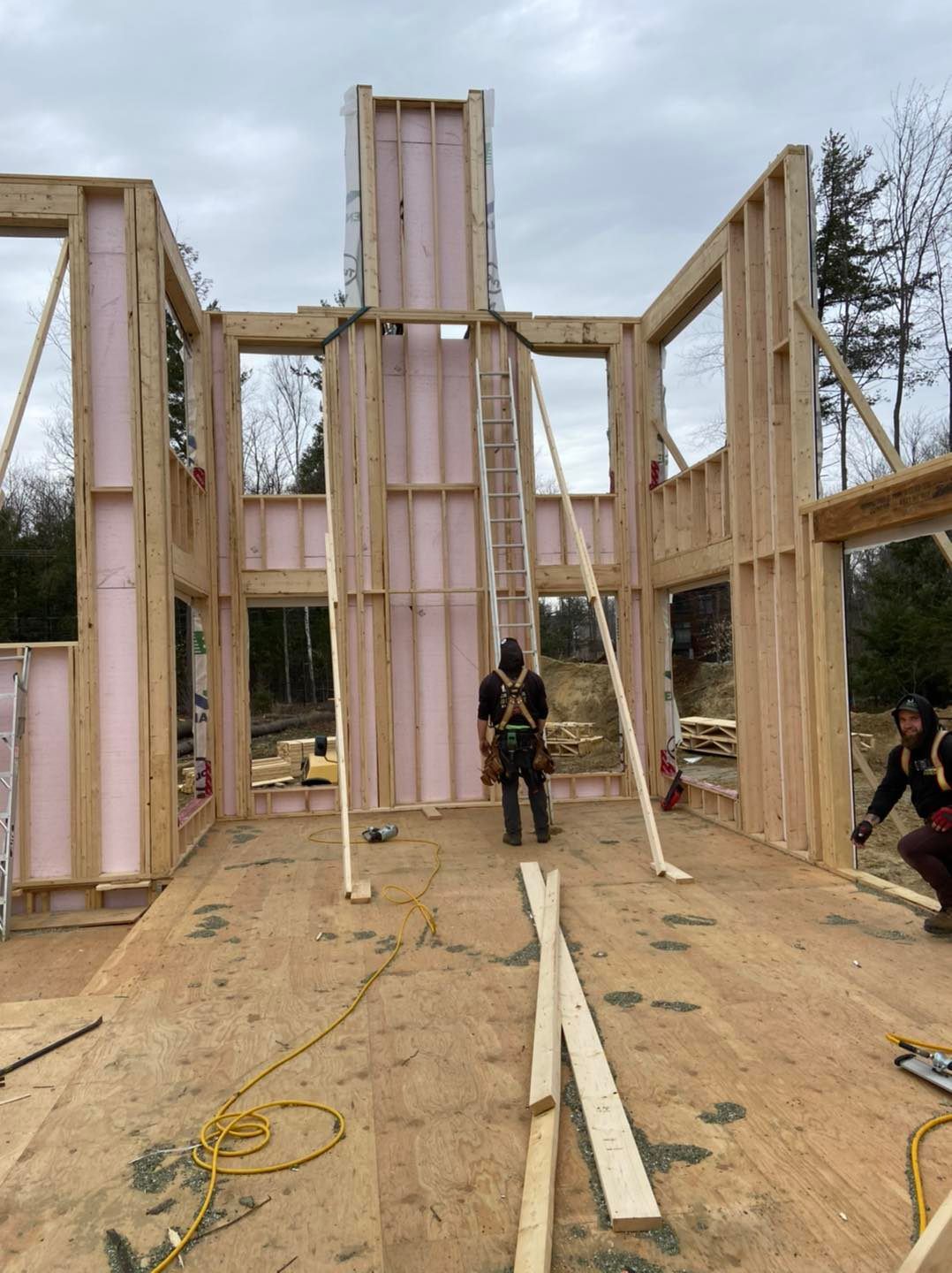 Des ouvriers du bâtiment construisent à l'extérieur une structure en bois pour une maison, en utilisant de l'isolant rose.