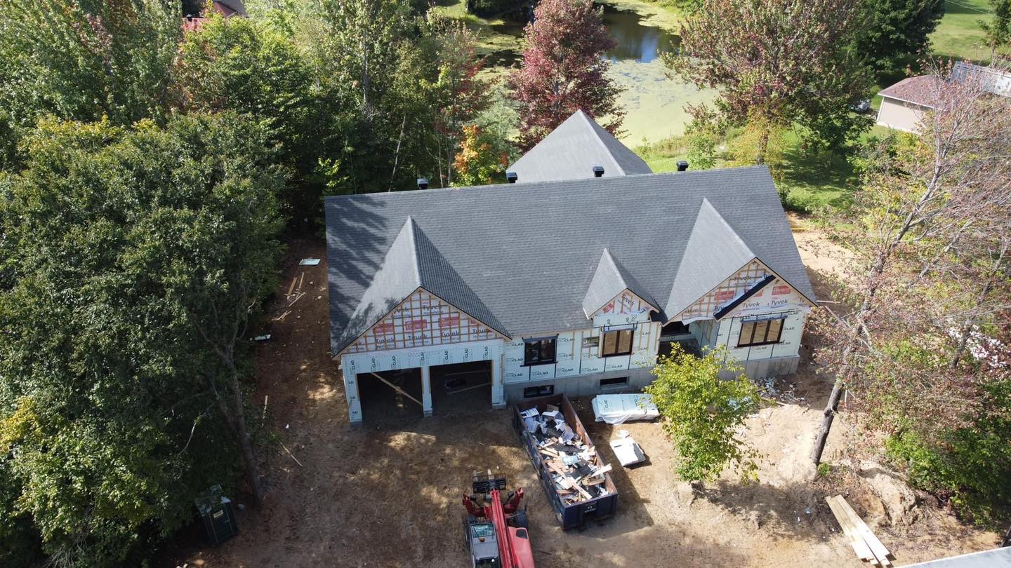 Maison neuve en construction avec toit noir et garage attenant.