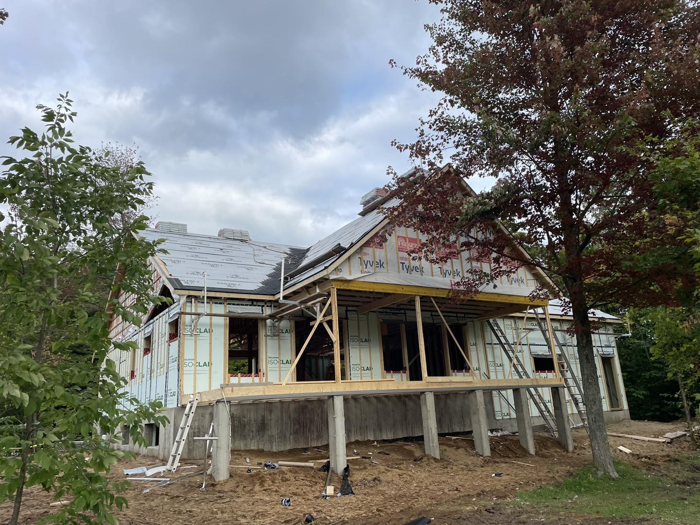 Maison en construction avec charpente apparente, isolation et toiture visibles, à l'extérieur par temps nuageux.