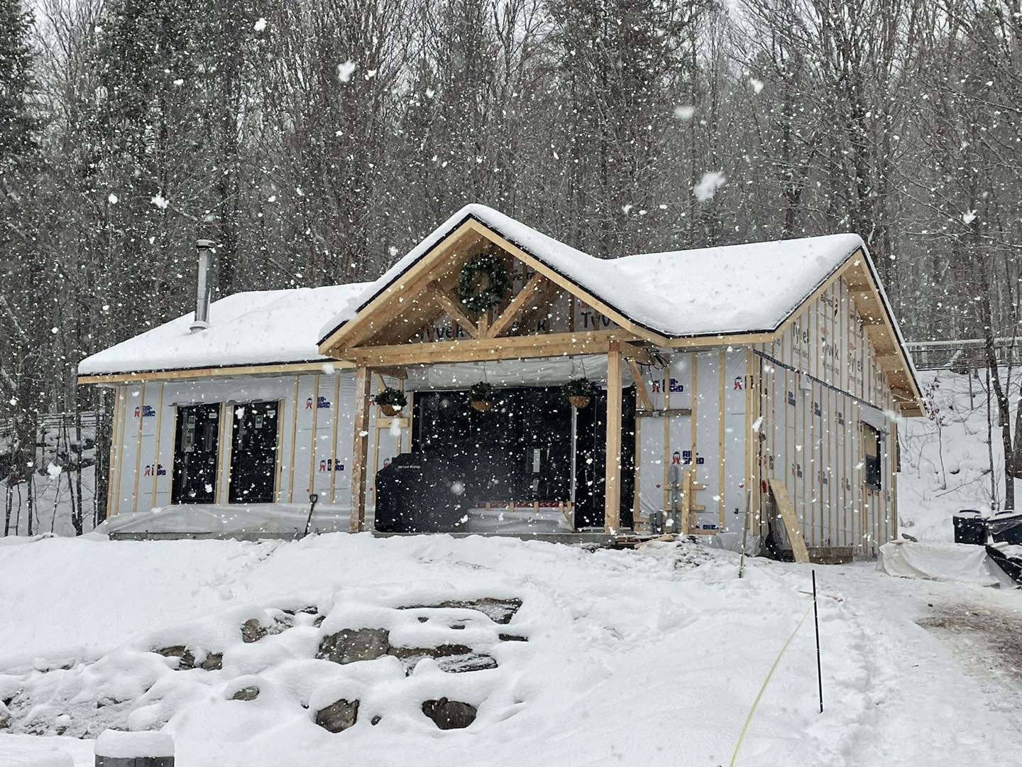 Une cabane en construction dans une forêt enneigée. La neige tombe sur le toit et le sol environnant.