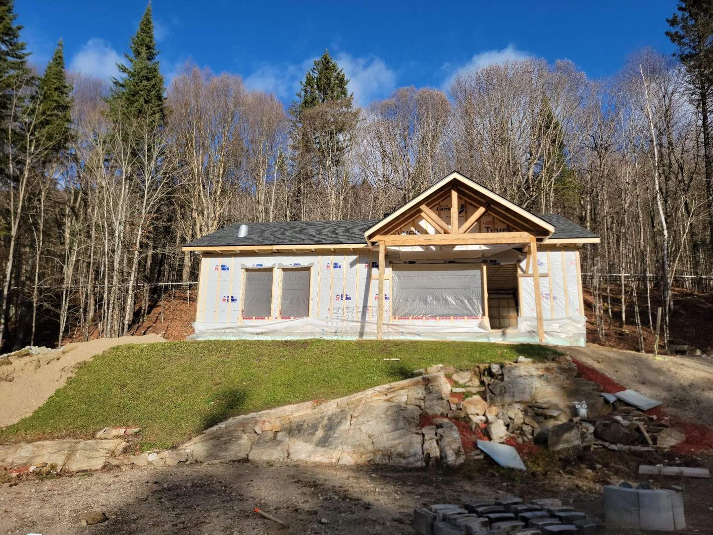 Construction d'une petite maison aux poutres apparentes, nichée dans un cadre forestier par une journée ensoleillée.