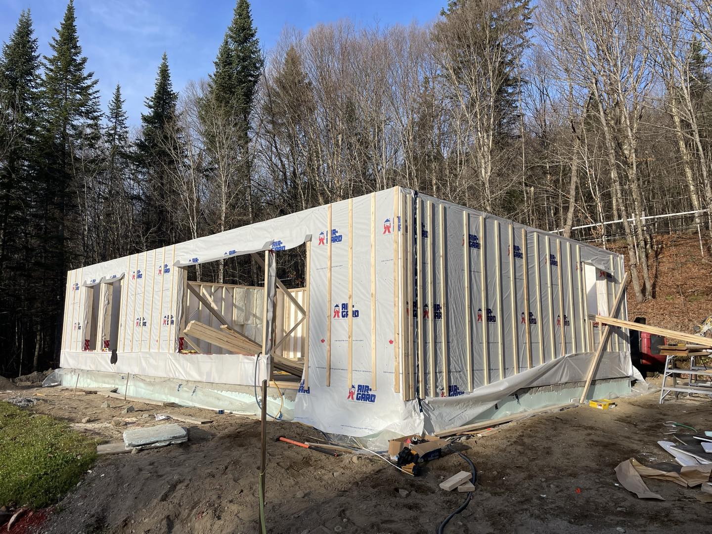 Construction de la structure en bois d'un bâtiment rectangulaire. Les murs sont partiellement revêtus ; forêt en arrière-plan.