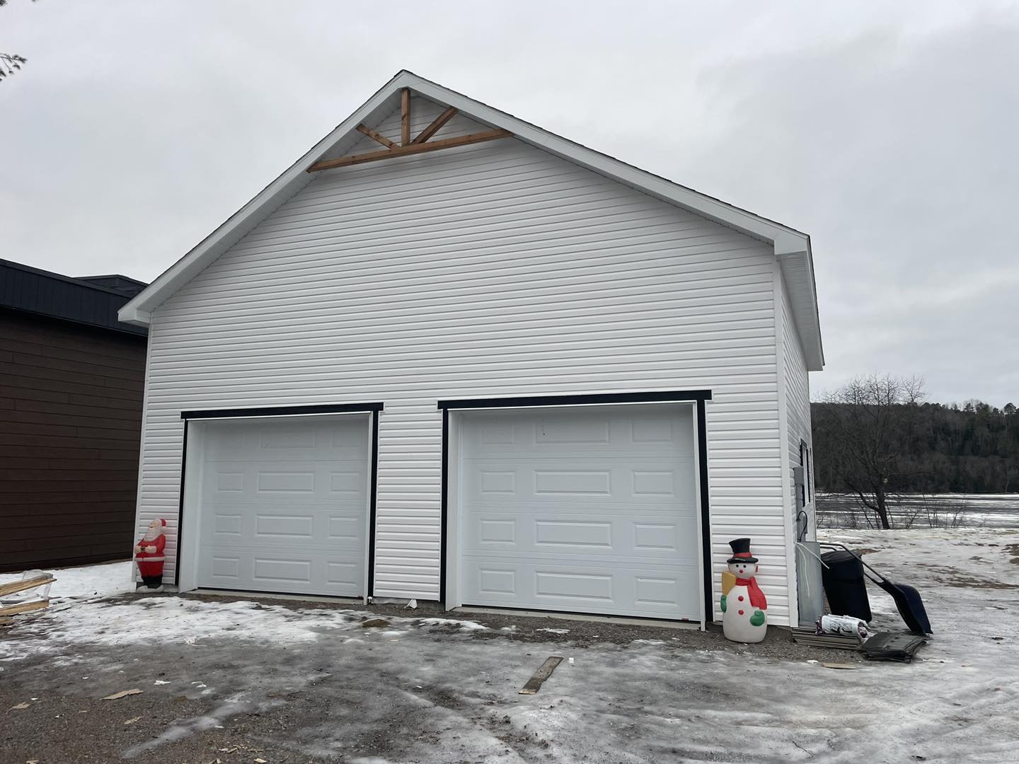 Garage blanc pour deux voitures, portes fermées, neige au sol, journée nuageuse.
