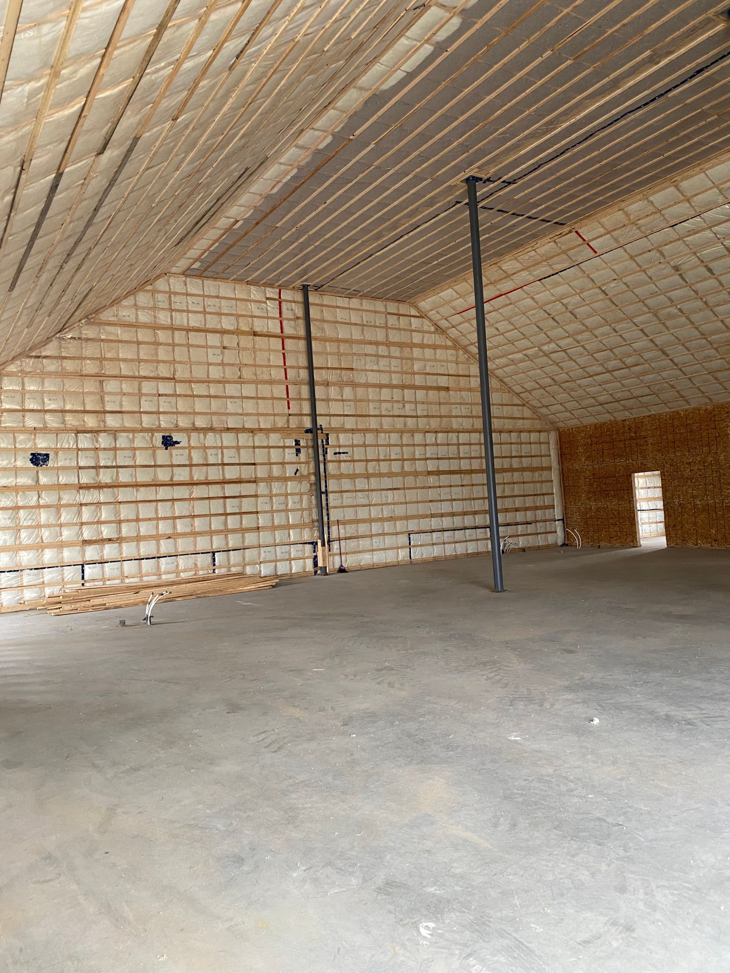 Intérieur d'un entrepôt vide avec sol en béton et murs/plafond en bois. Deux poutres de soutien sont visibles.