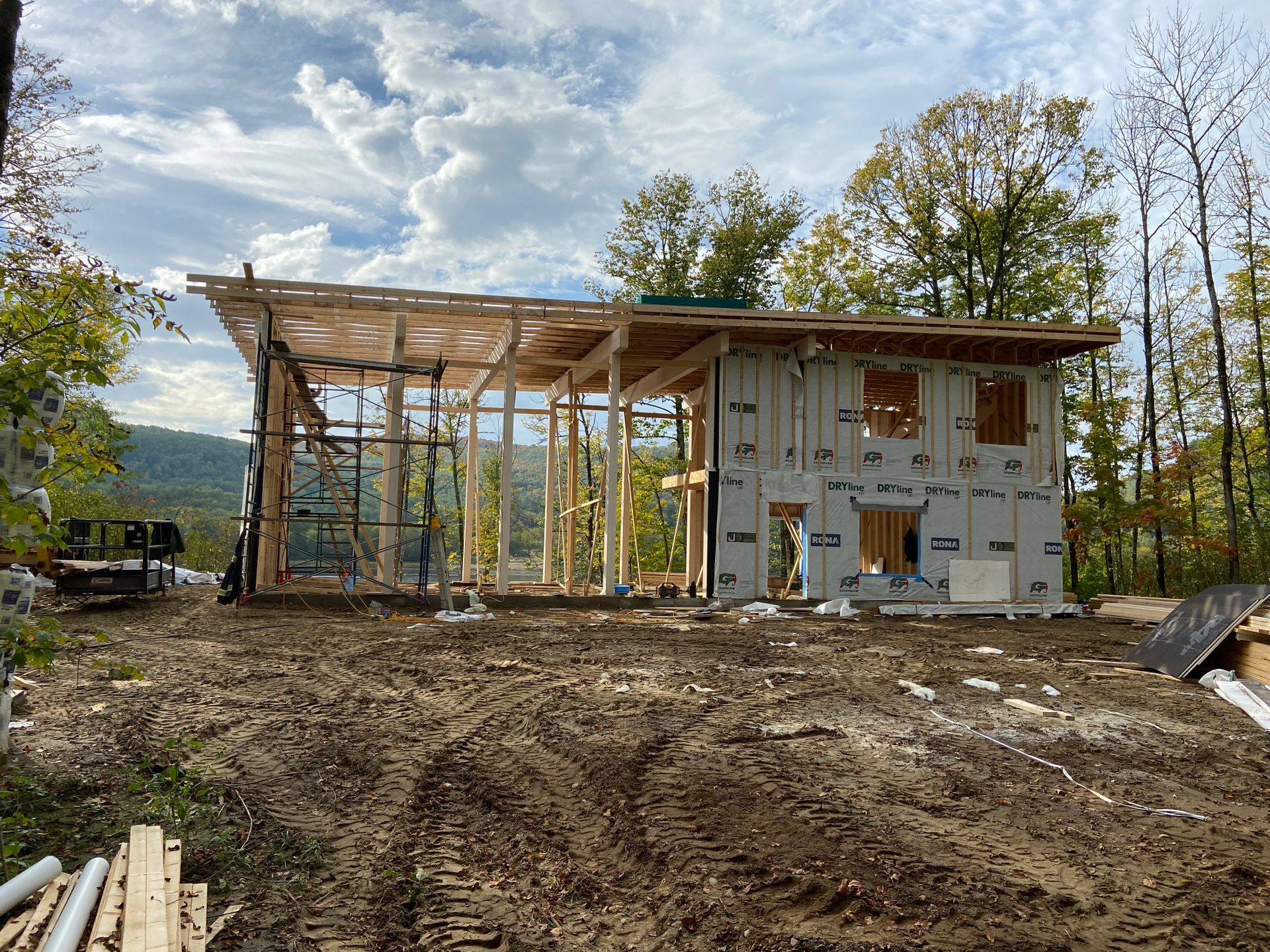 Construction d'une maison moderne, avec ossature bois, bardage et toiture partielle, située dans une zone boisée.