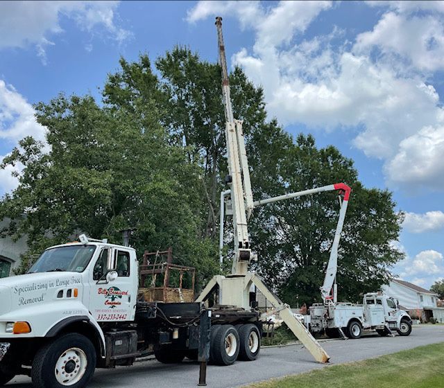 White drilling rig trucks parked on a road beside trees under a partly cloudy sky