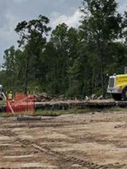 Construction site with bulldozer, orange safety fencing, and trees in the background