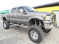 Lifted gray pickup truck with large off-road tires parked outside a building