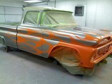 Classic car in paint booth, masked with plastic and orange-gray spray paint.