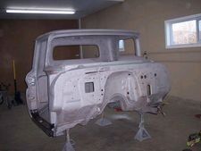 White truck cab body in a garage, primed and raised on stands during restoration work