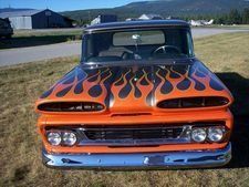 Front view of a black and orange custom pickup truck with flame paint and chrome grille on grass outdoors